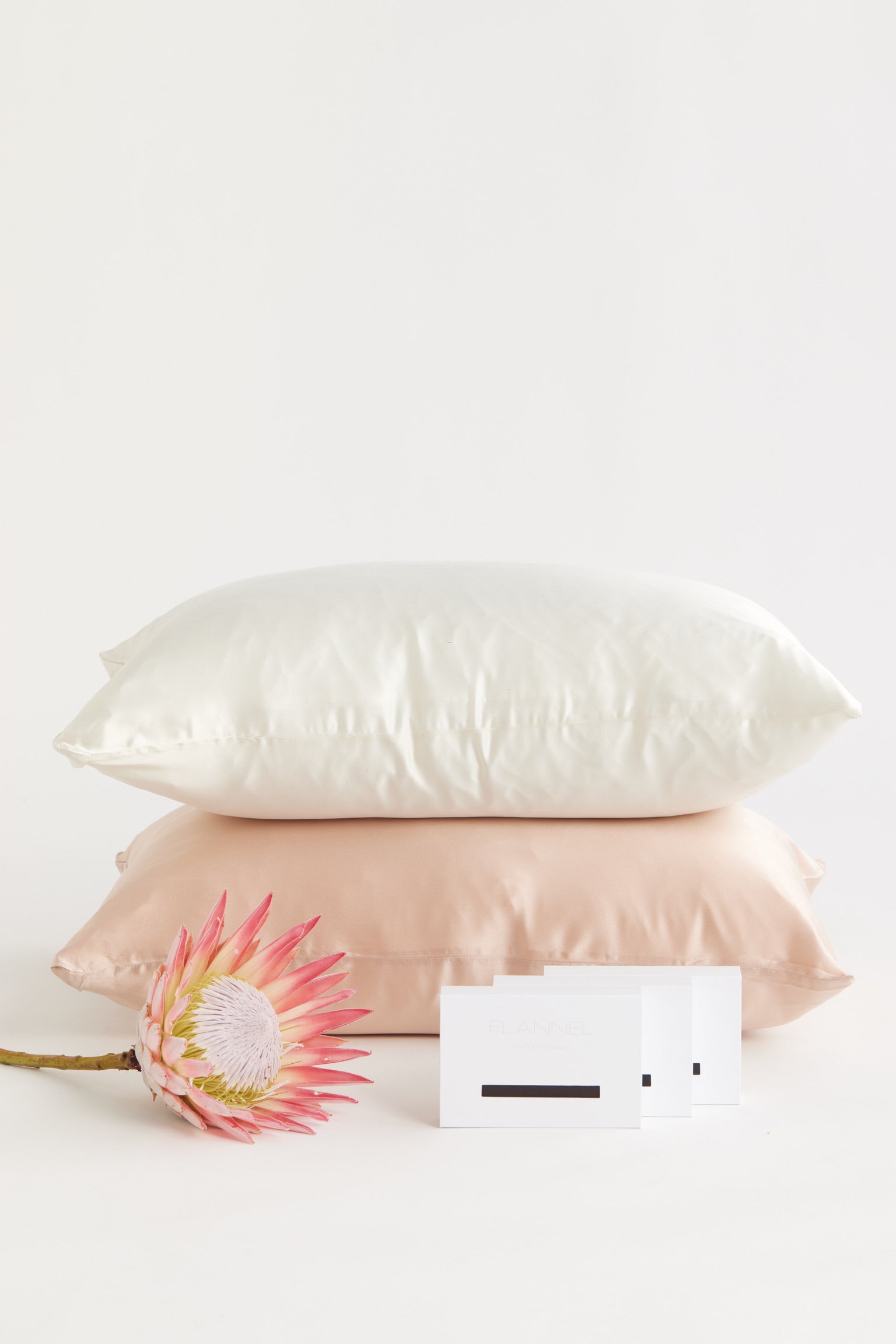 Image of a milk and rose coloured silk pillowcases stacked on top of each other.