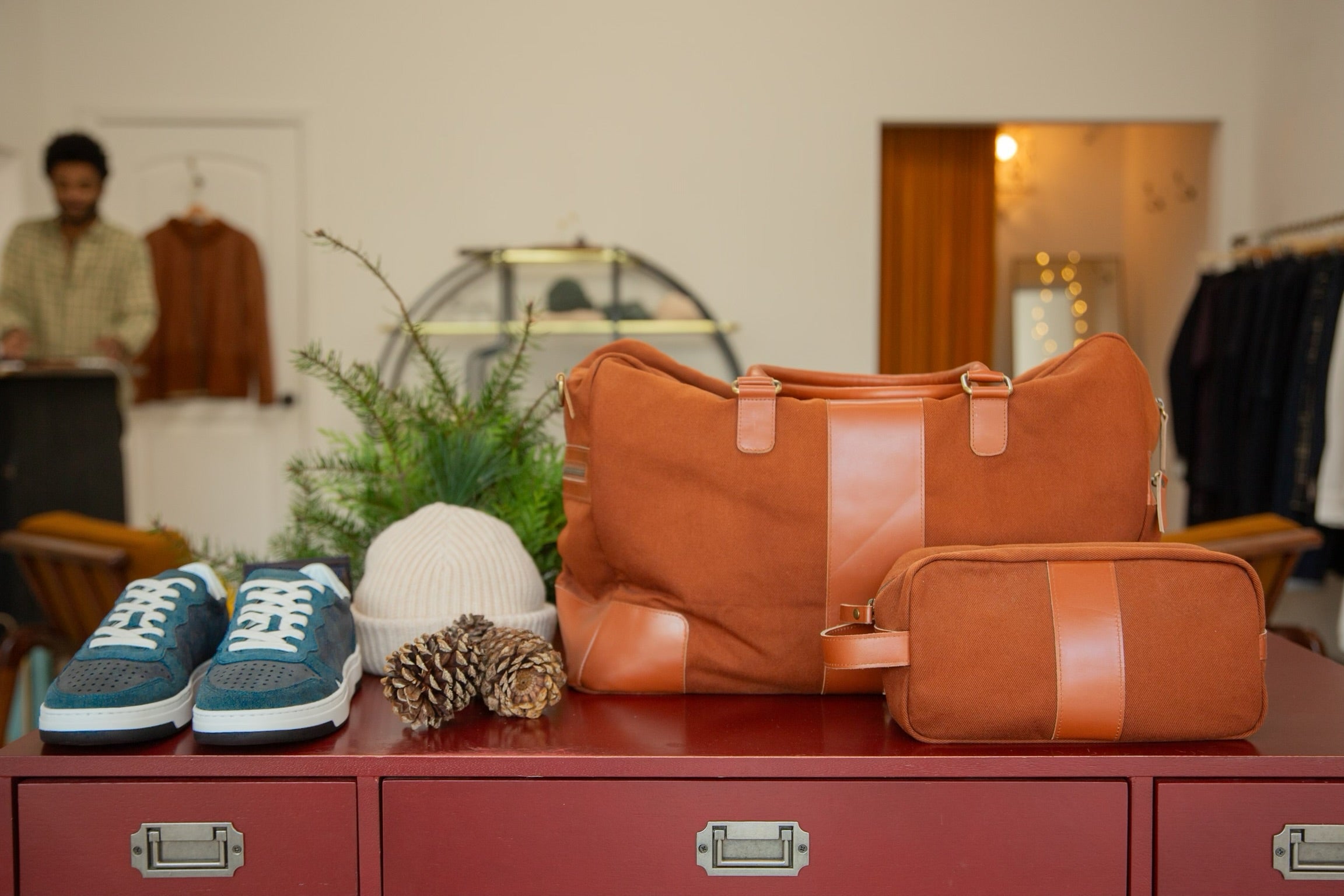In situ image of a selection of mens accessories such as an overnight bag, and toiletry bag, sneakers and a beanie.