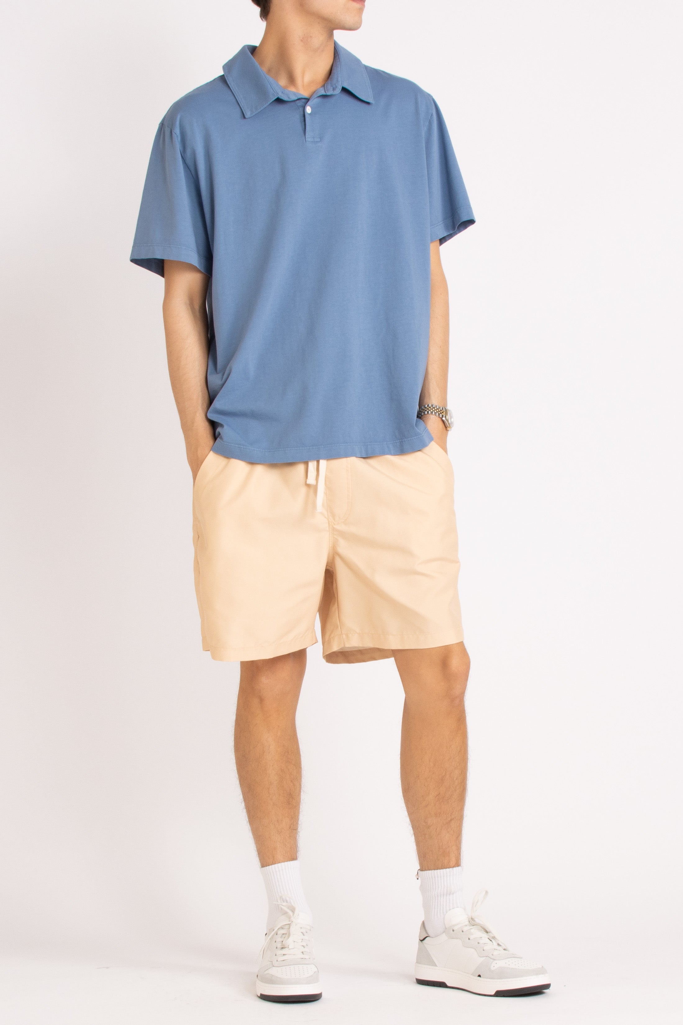 model wearing blue cotton polo shirt, light sand shorts and white sneakers on a white background, front view