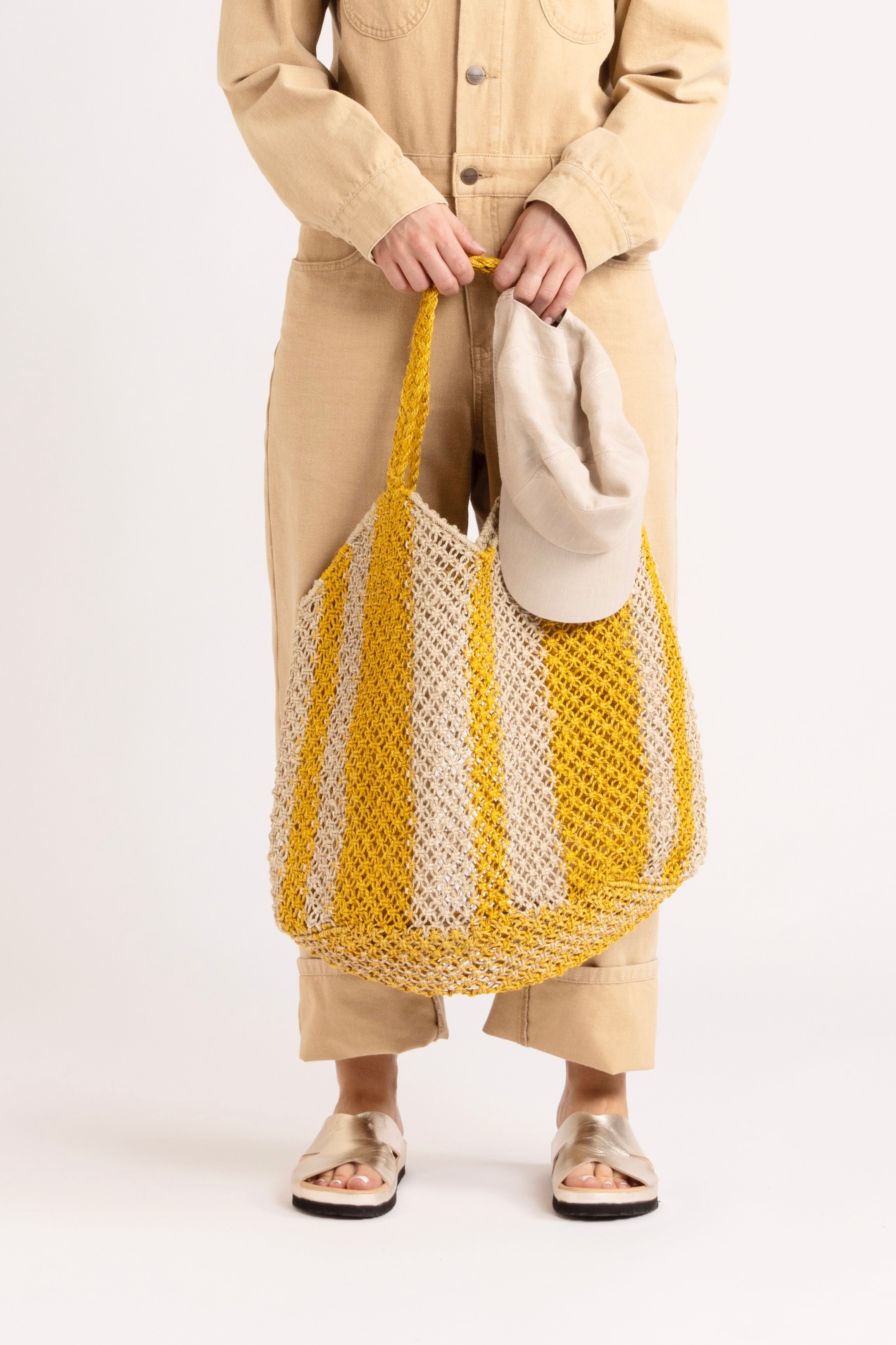 Model wearing a cream jumpsuit holding a yellow and white braided raffia bag.