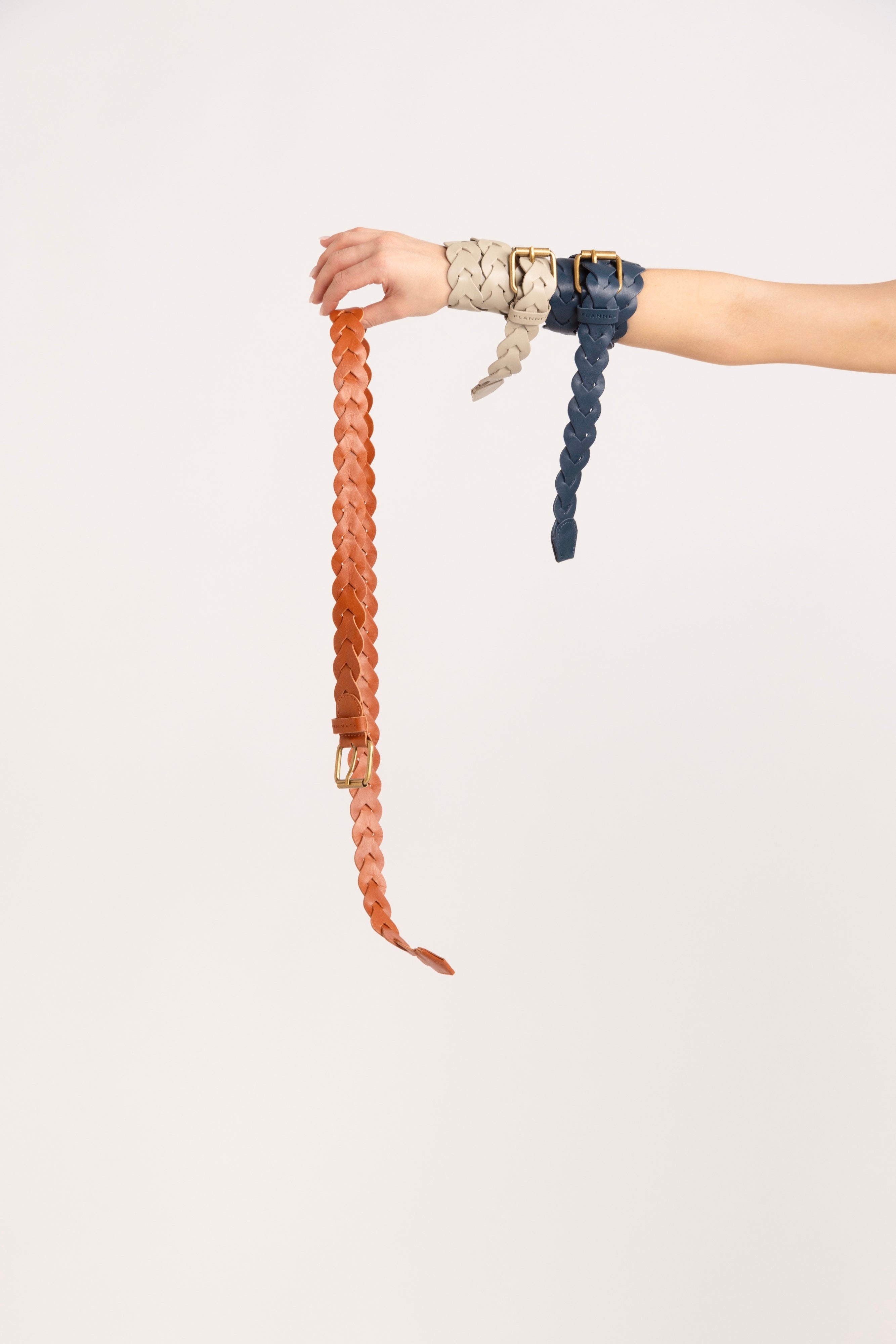Model holding a selection of orange, cream and navy braided belts.