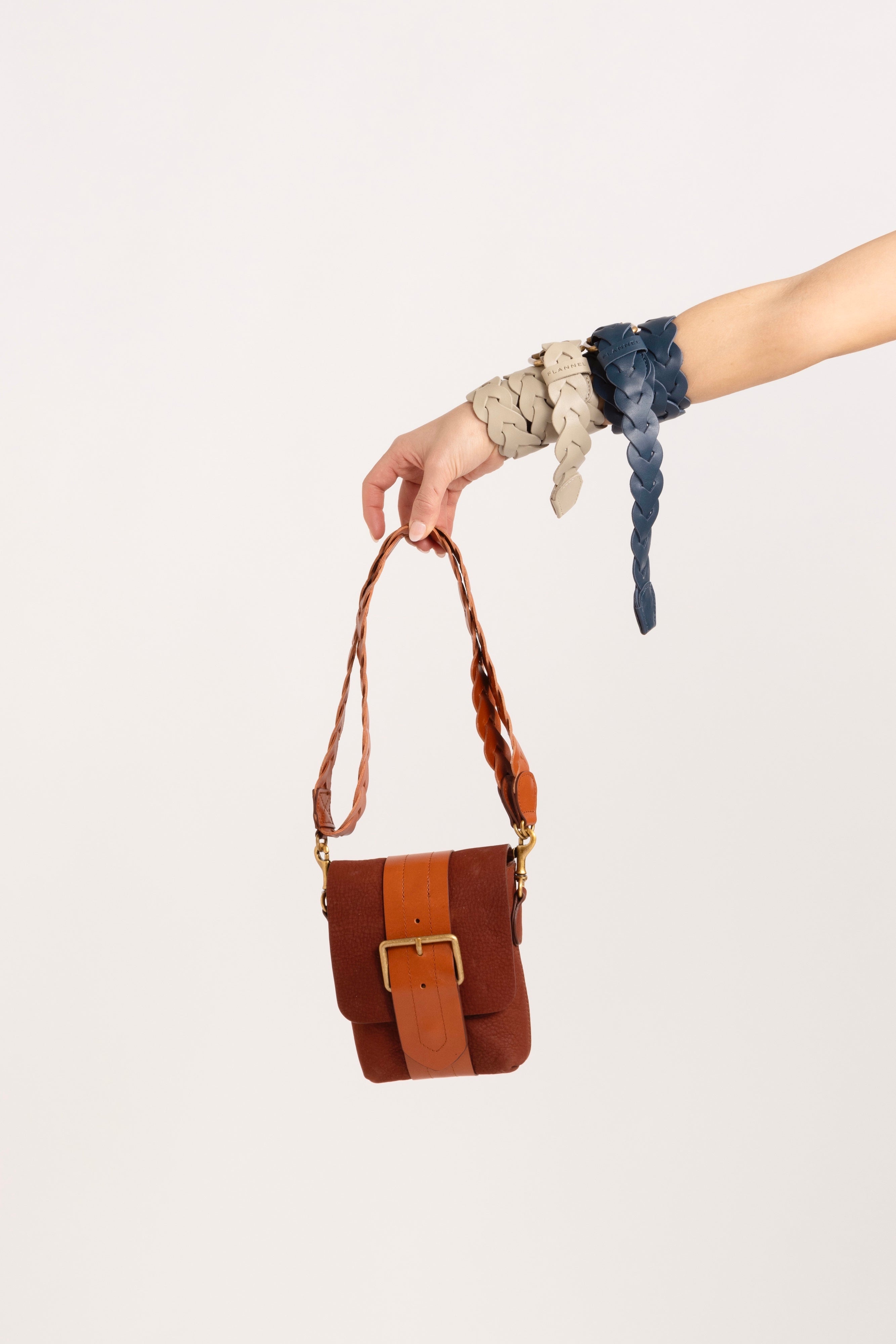 Model holding an orange pouch with a cream and navy belt wrapped around her wrist.