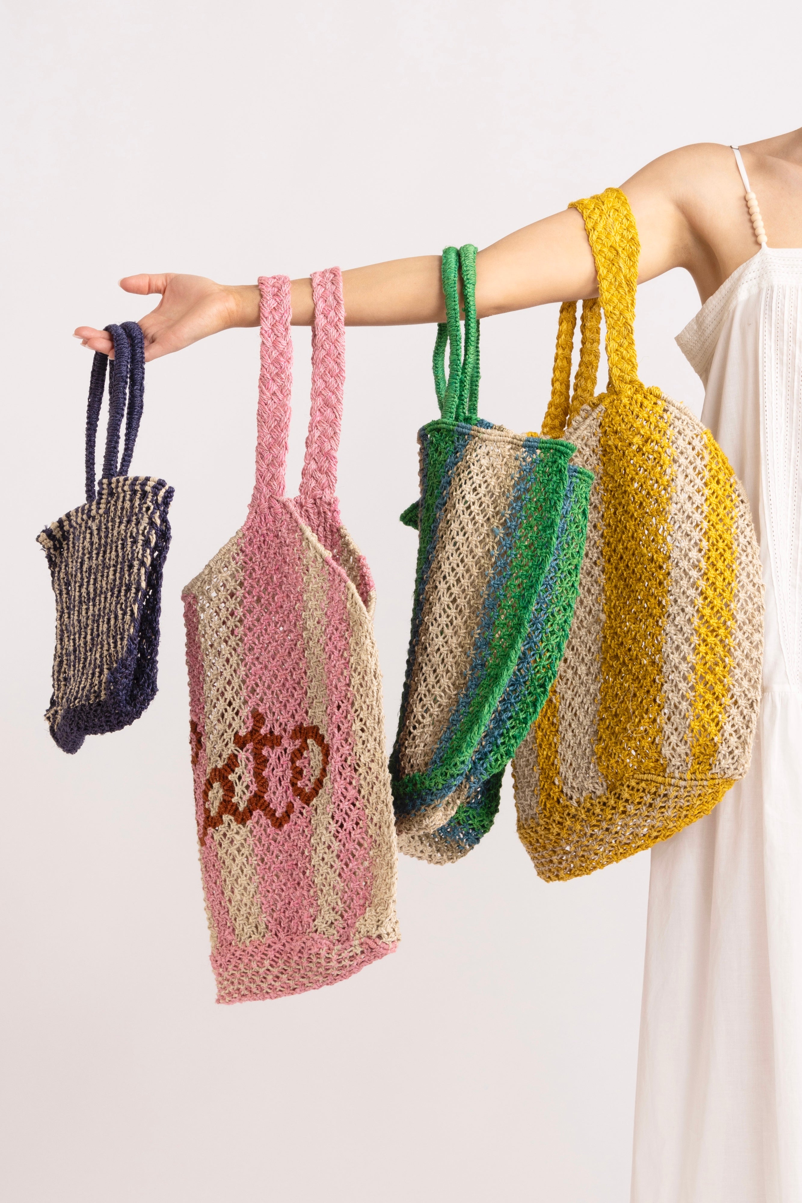 Model holding a selection of bright coloured braided raffia tote bags.