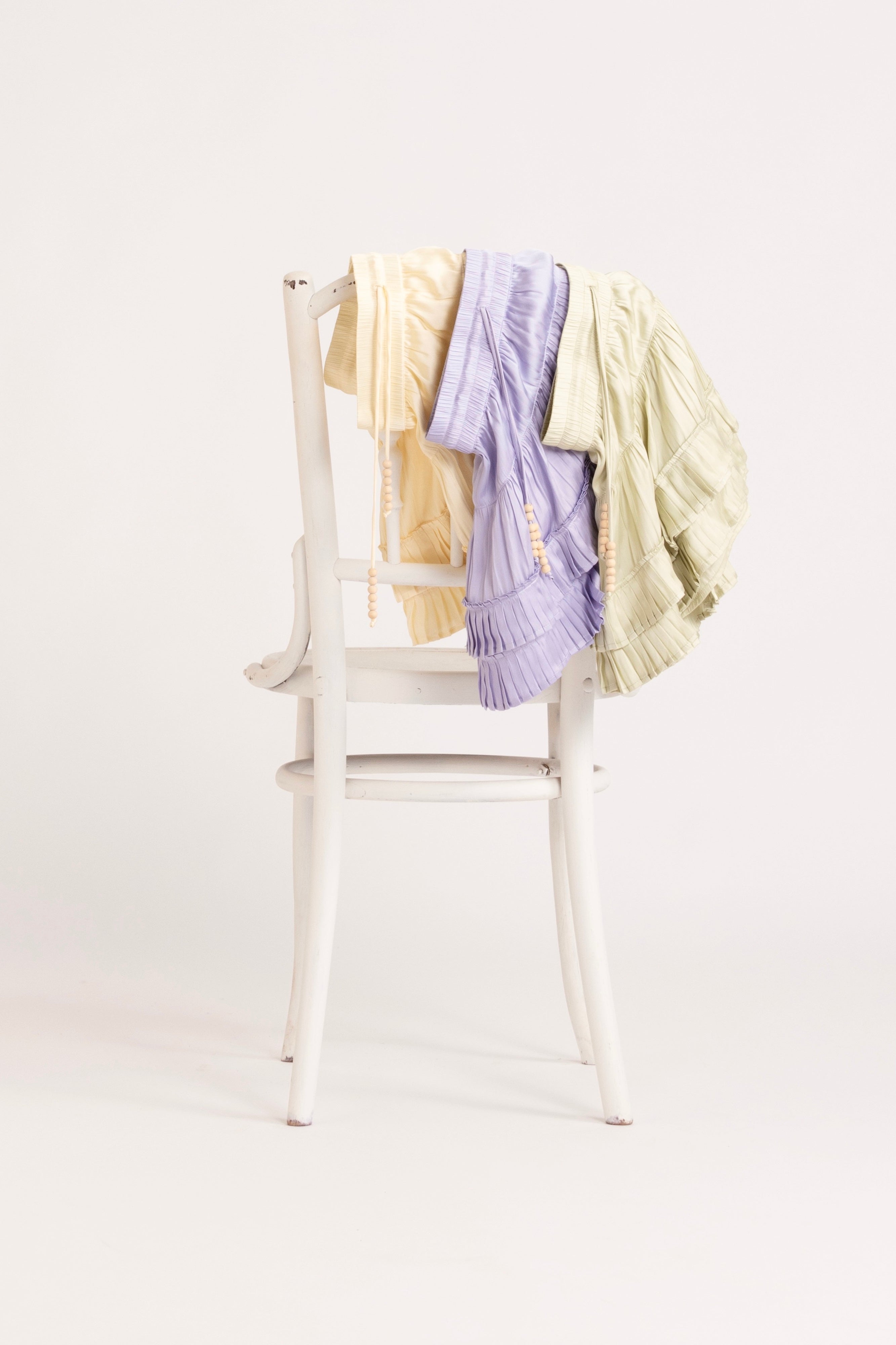 A selection of butter, lilac and pistachio coloured frill short hanging on a chair.