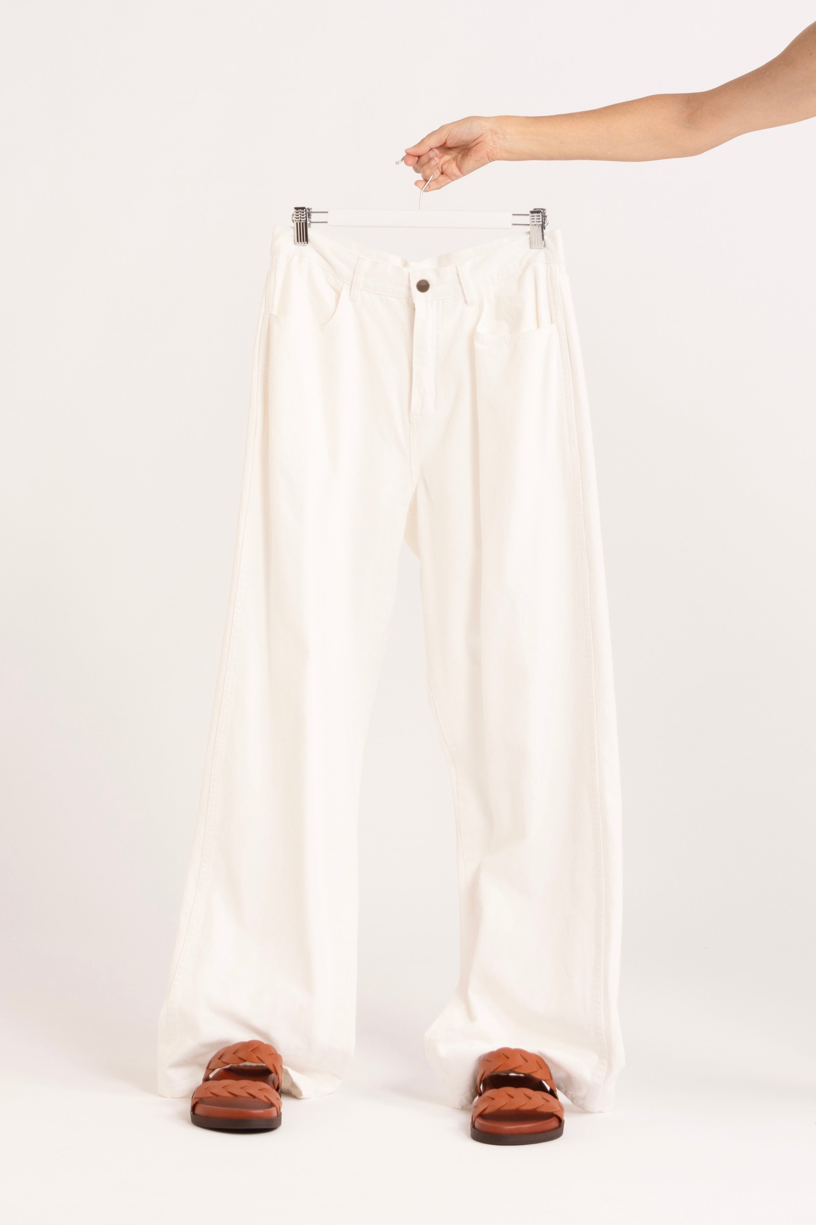 Image of model holding a pair of white jeans, with orange braided slides.
