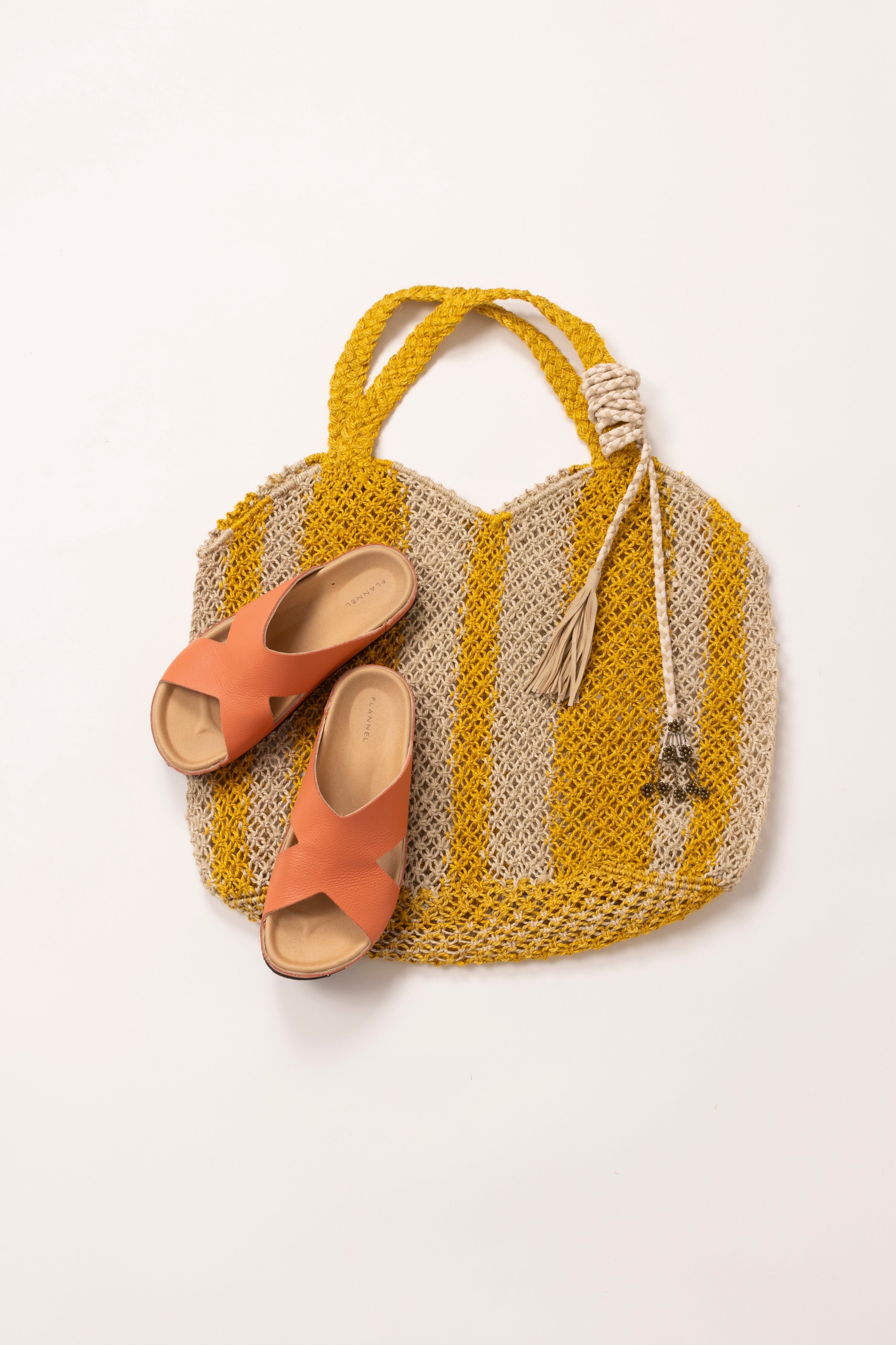 In situ image of a yellow and white striped raffia with peach leather slides placed on top.