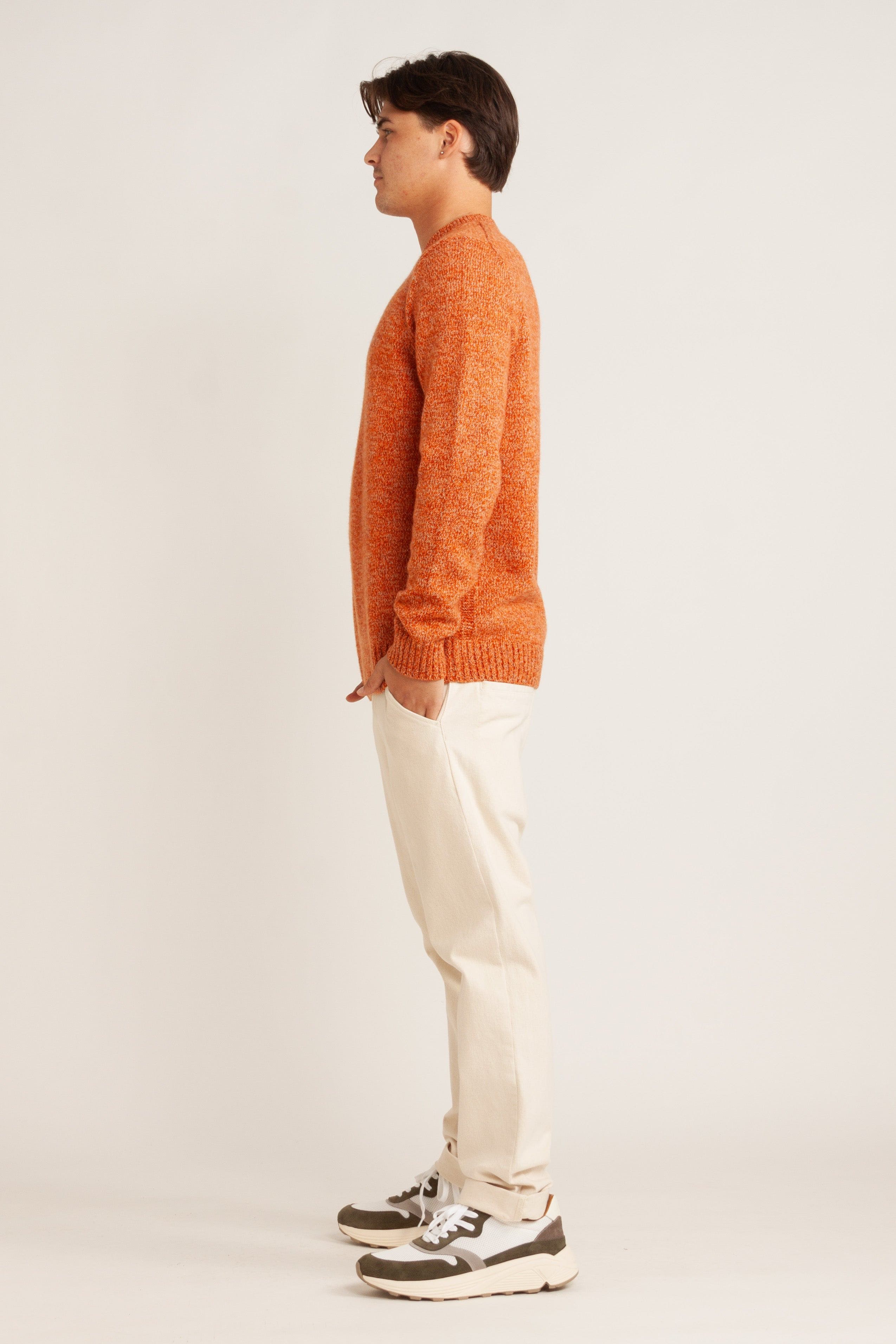 Model wearing orange knit sweater, natural linen pant and green suede/mesh sneakers, side view
