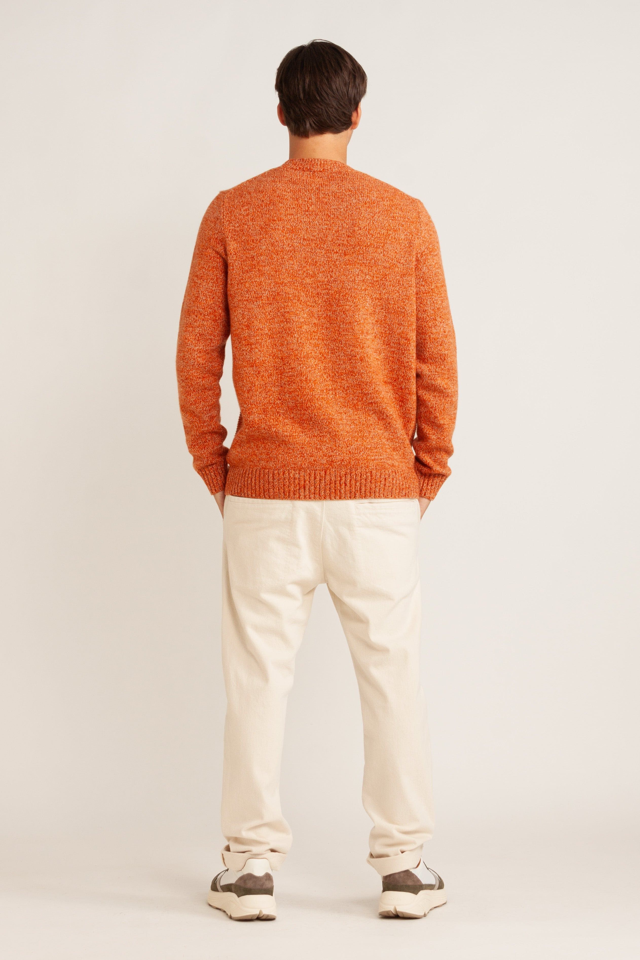 Model wearing orange knit sweater, natural linen pant and green suede/mesh sneakers, back view
