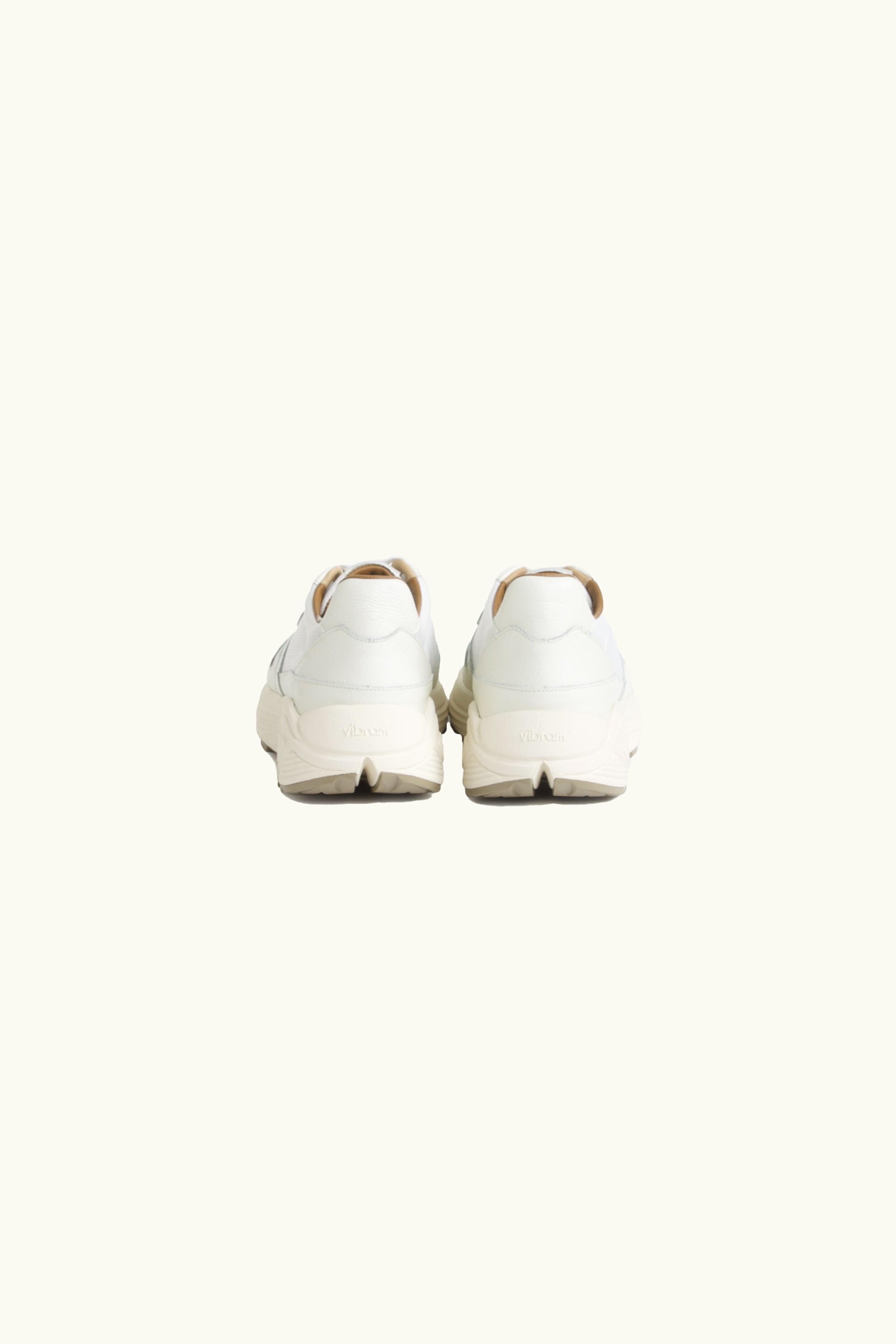 Pair of white shoes on a light beige background, back view