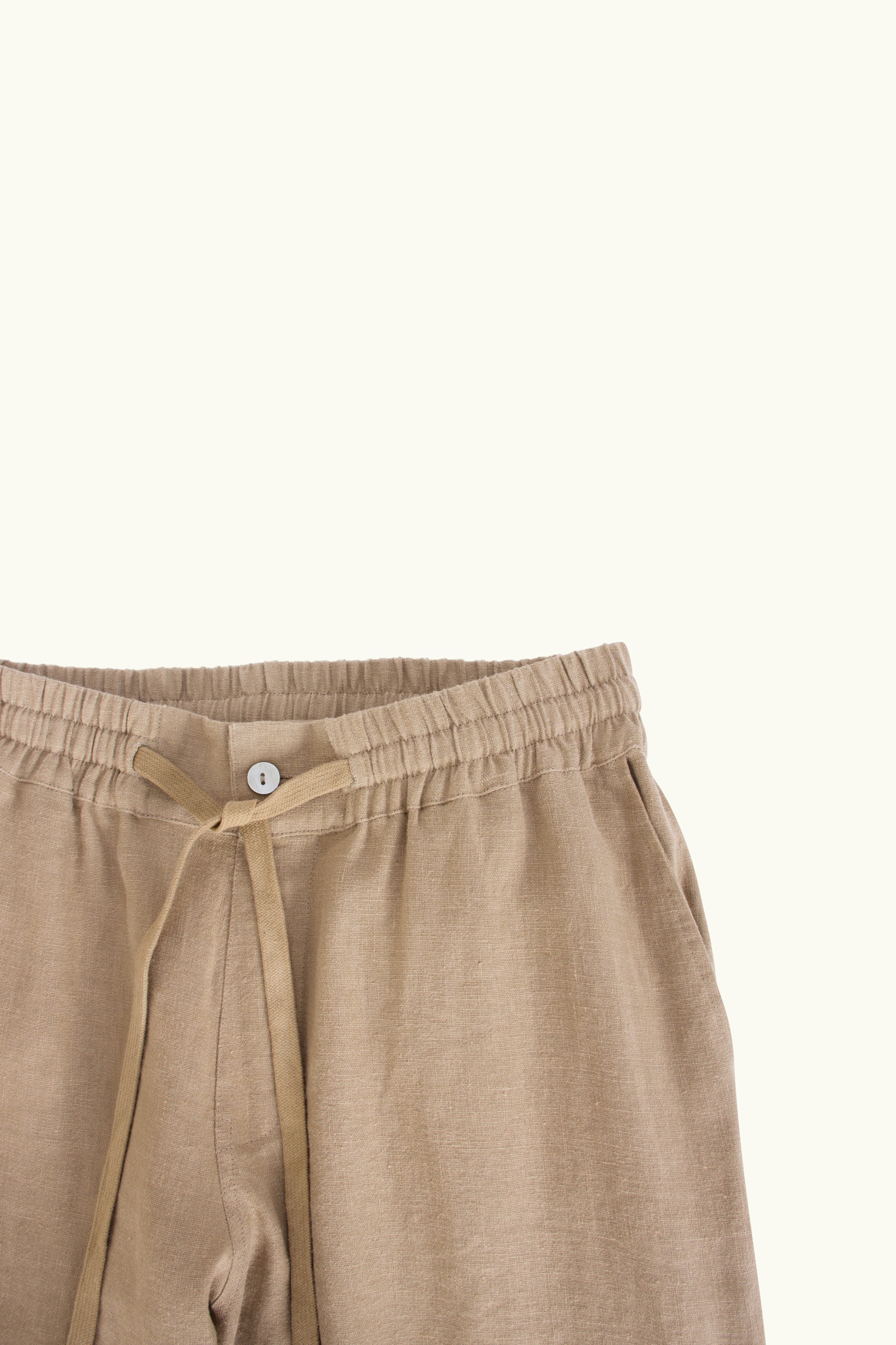 Close up of mocha linen pants with a tie detail on a white background