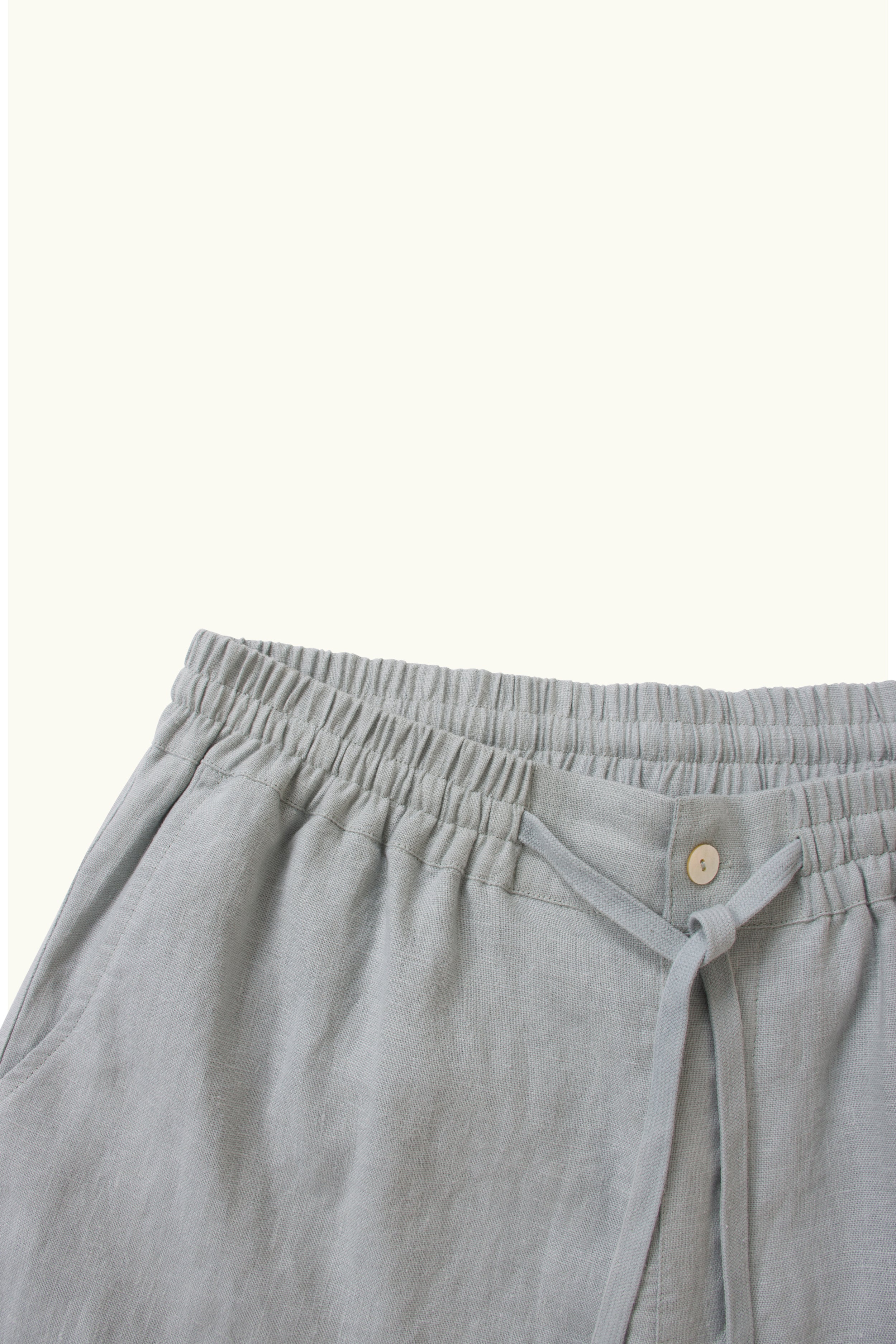 Close-up of light blue linen short with a button on a white background