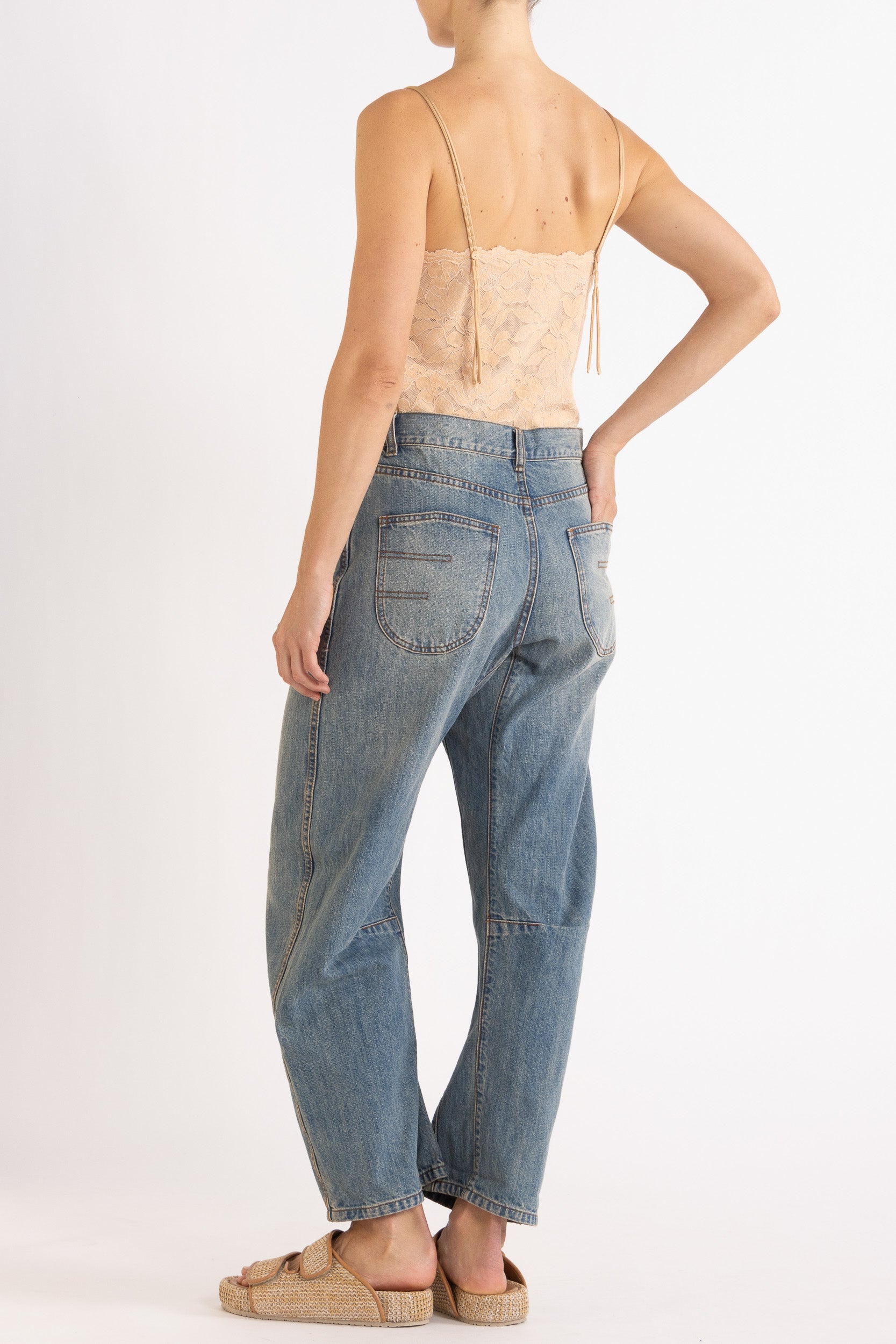 Woman wearing a floral lace camisole in biscuit colour way paired with denim bow-leg jeans with a white background
