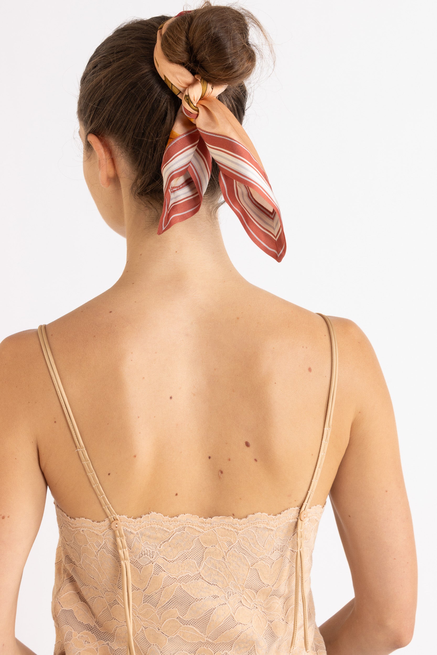 Woman wearing a beige lace camisole with a patterned headscarf on a white background