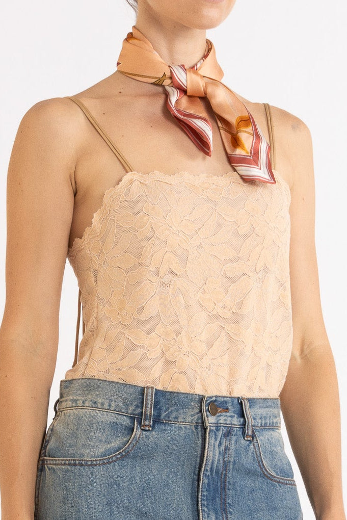 Person wearing a beige lace camisole, decorative scarf and blue jeans on a white background