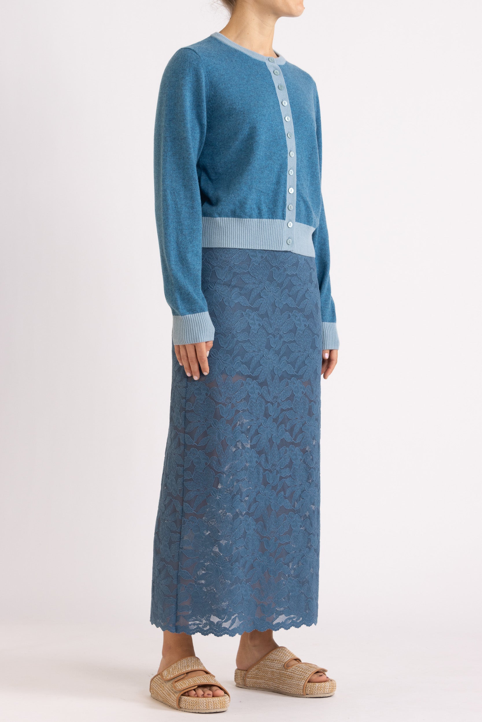 Woman wearing a two toned blue cashmere cardigan paired with blue floral maxi skirt with a white background