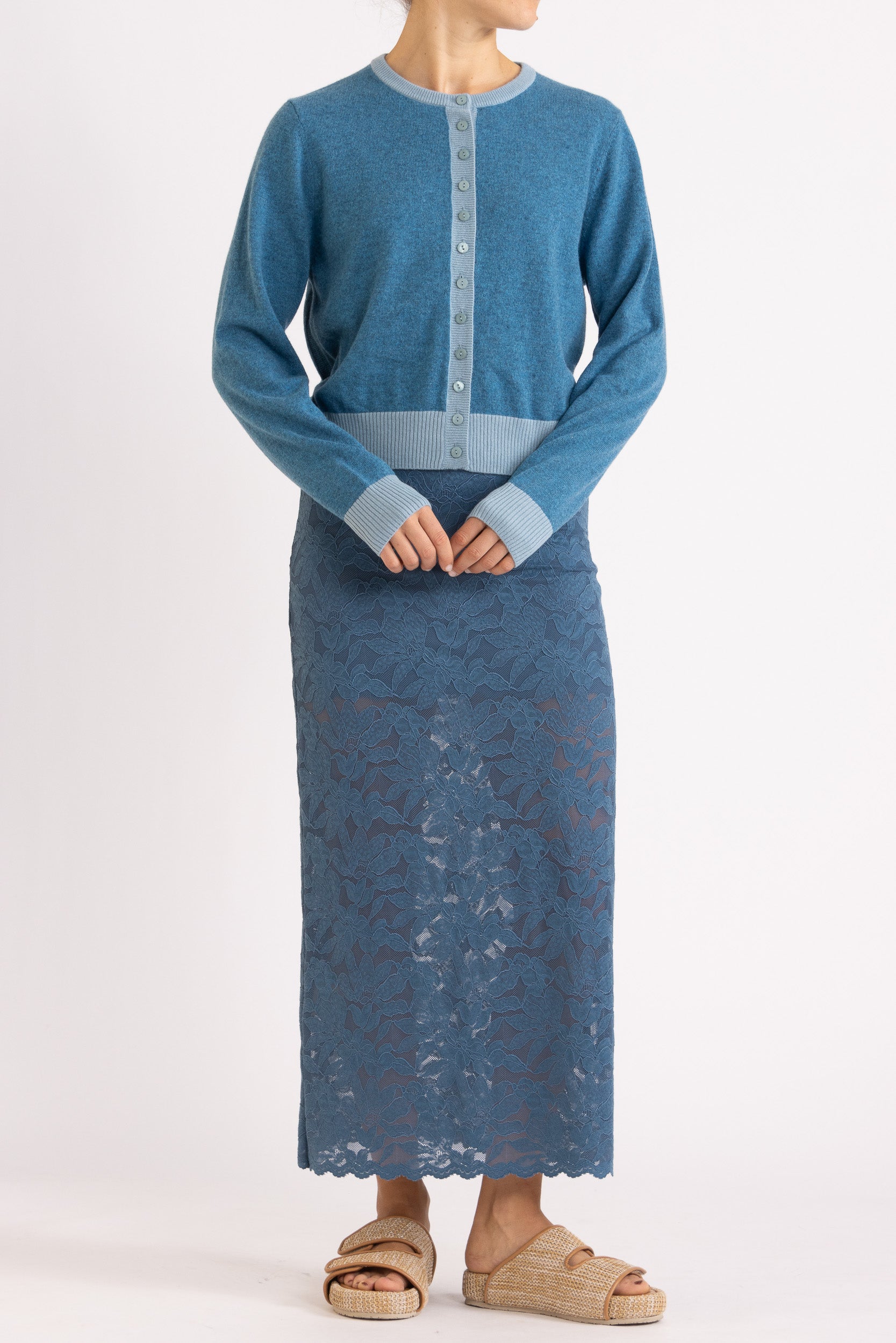 Woman wearing a two toned blue cashmere cardigan paired with blue floral maxi skirt with a white background