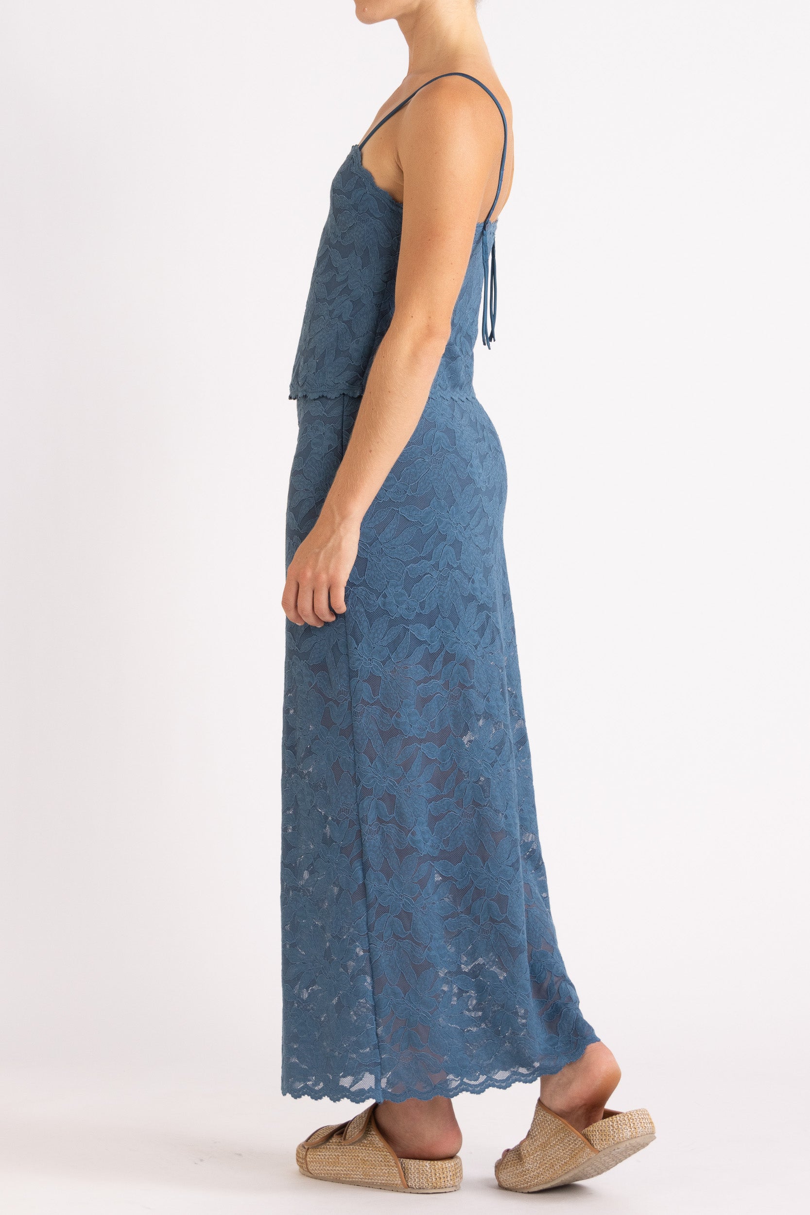 Woman wearing matching blue floral lace camisole top and maxi skirt with a white background