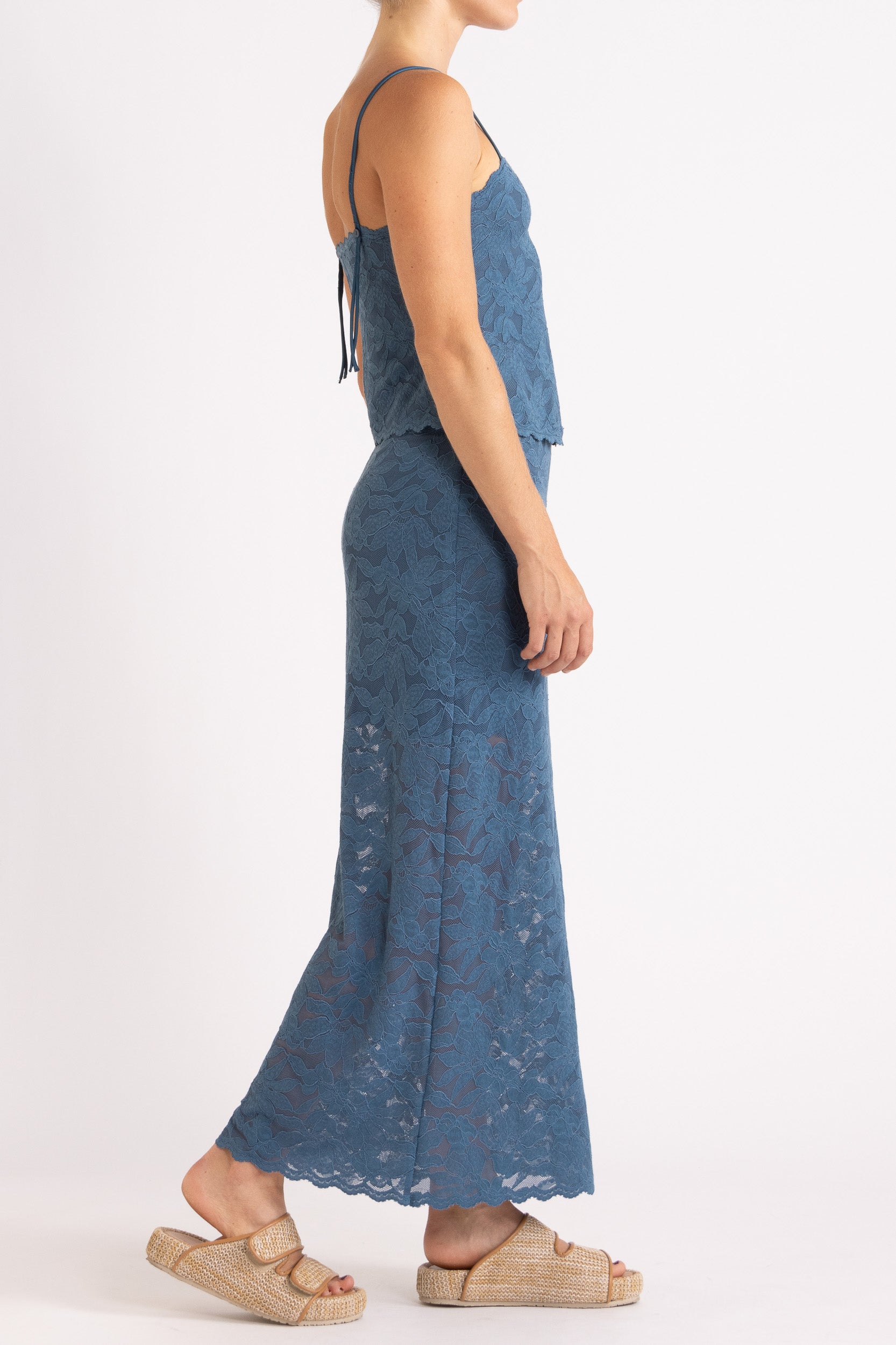 Woman wearing matching blue floral lace camisole top and maxi skirt with a white background