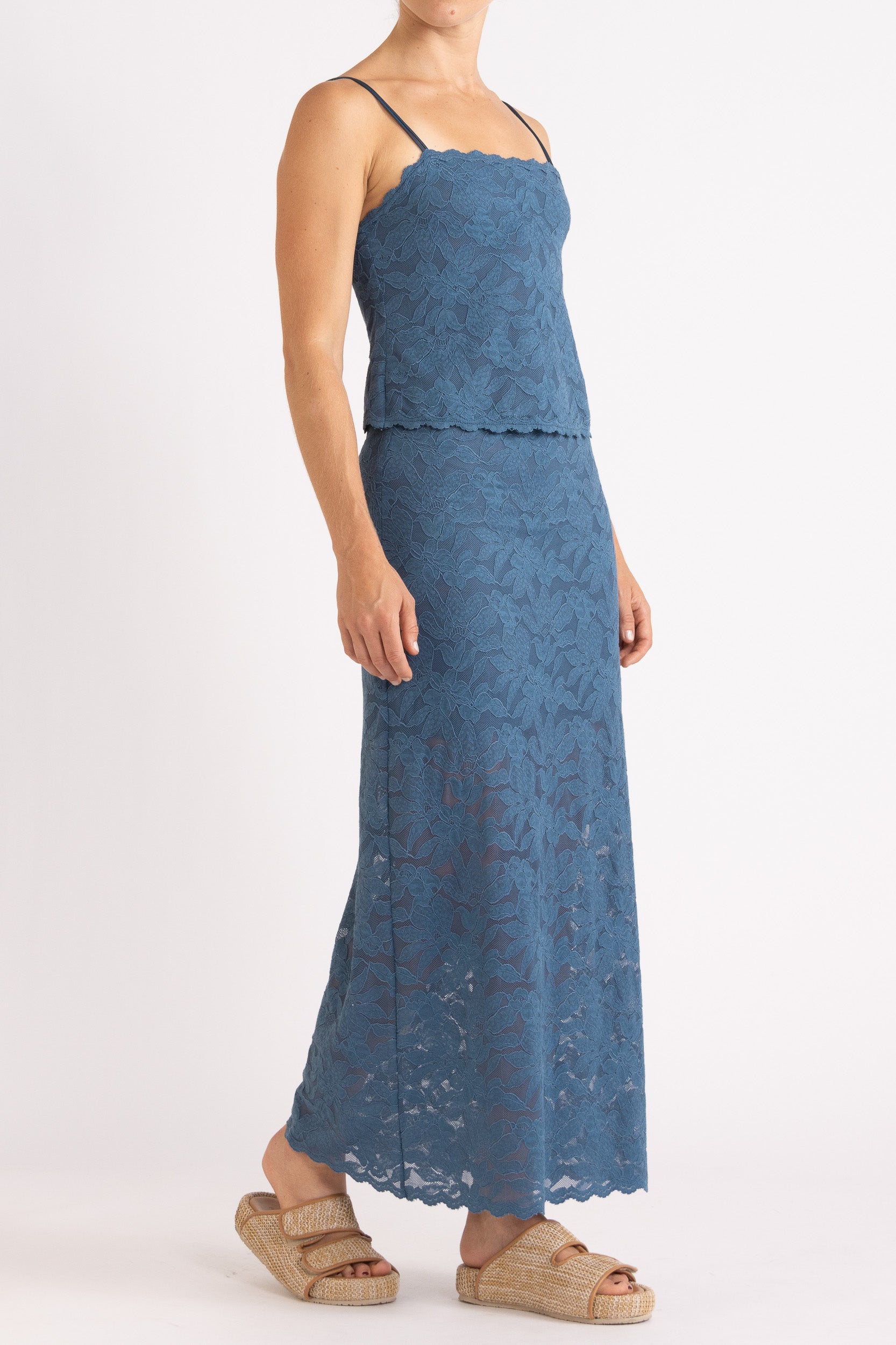 Woman wearing matching blue floral lace camisole top and maxi skirt with a white background