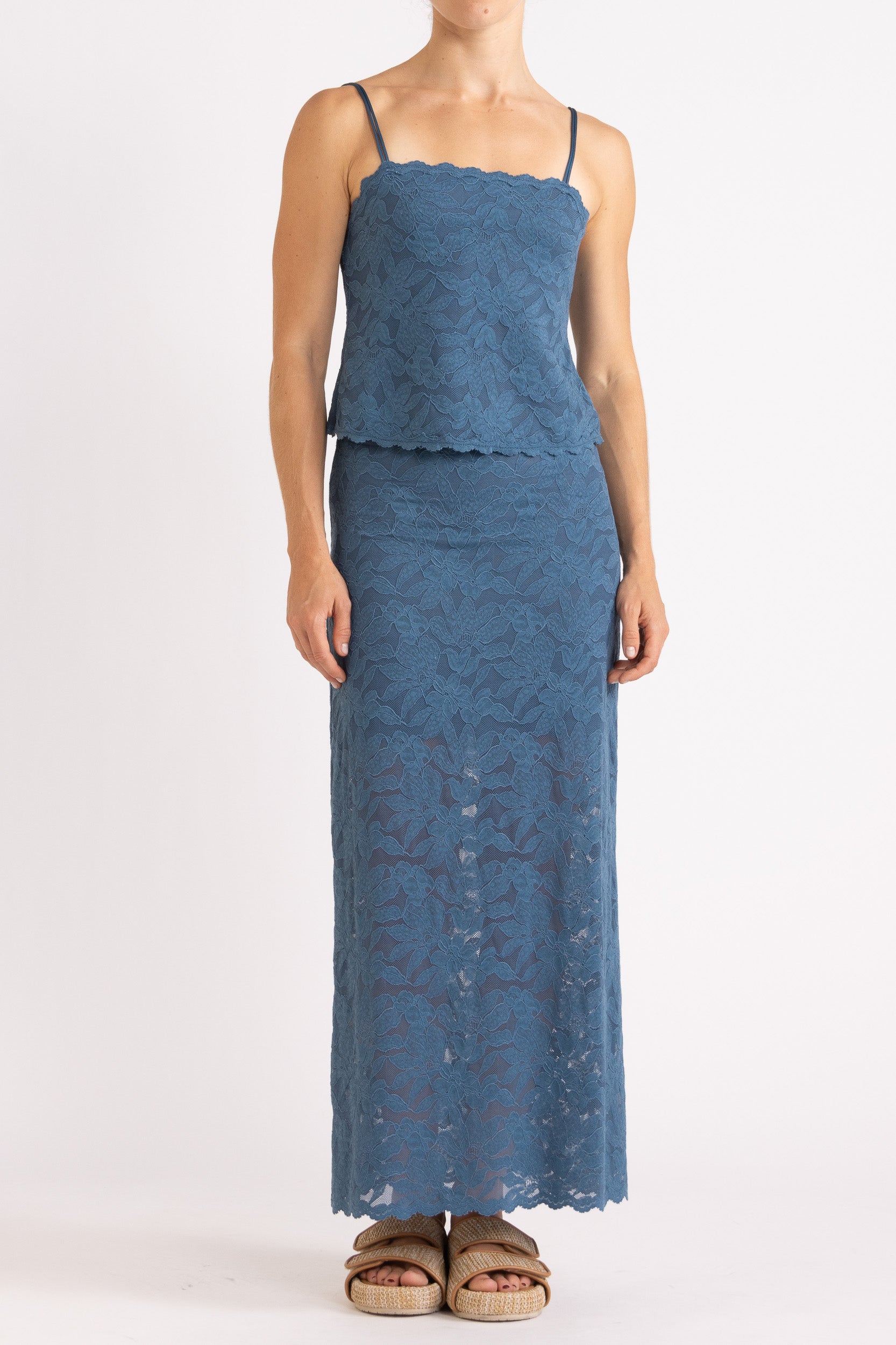 Woman wearing matching blue floral lace camisole top and maxi skirt with a white background
