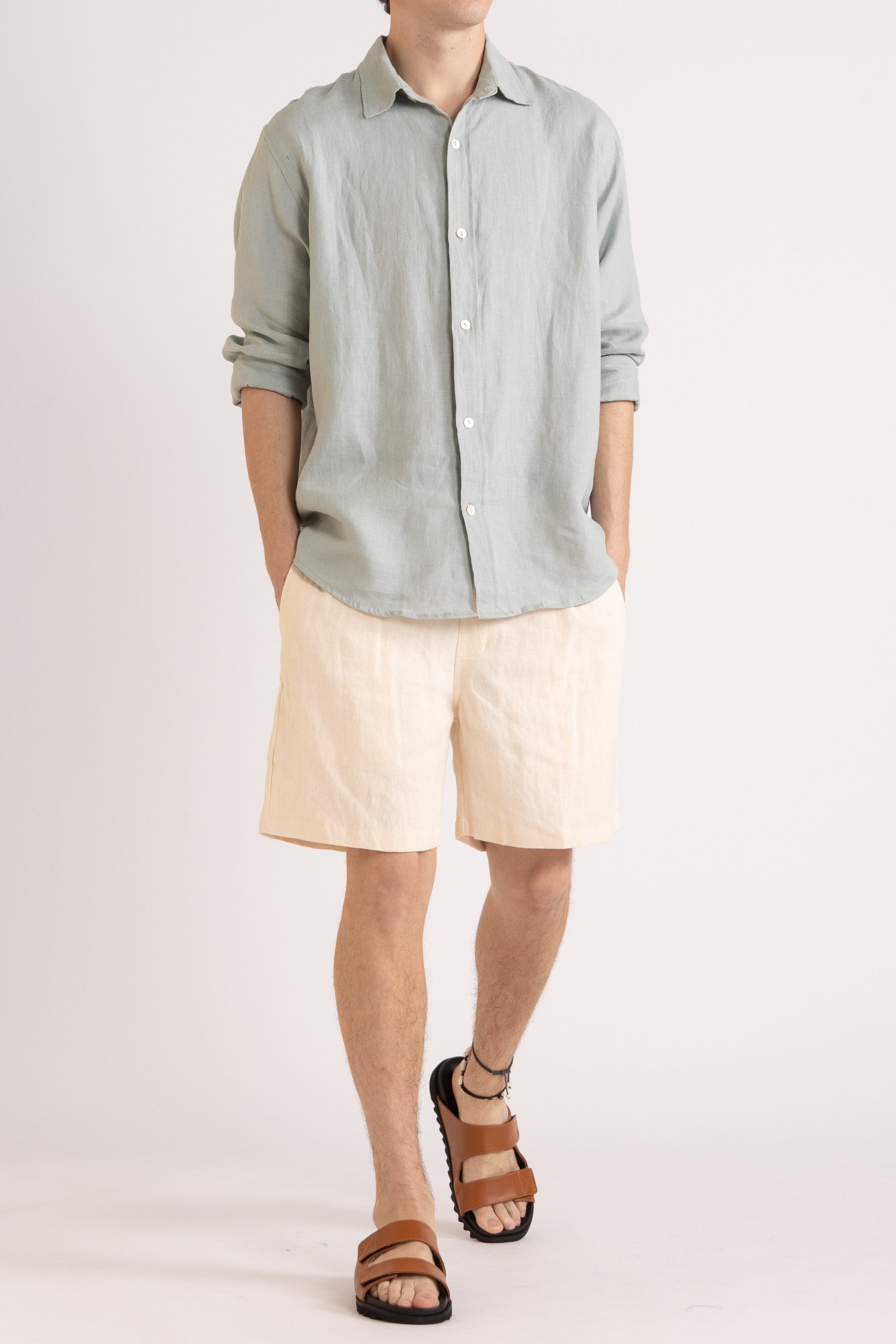 Person wearing a light blue long sleeve linen button-up shirt and natural linen shorts on a white background, front view