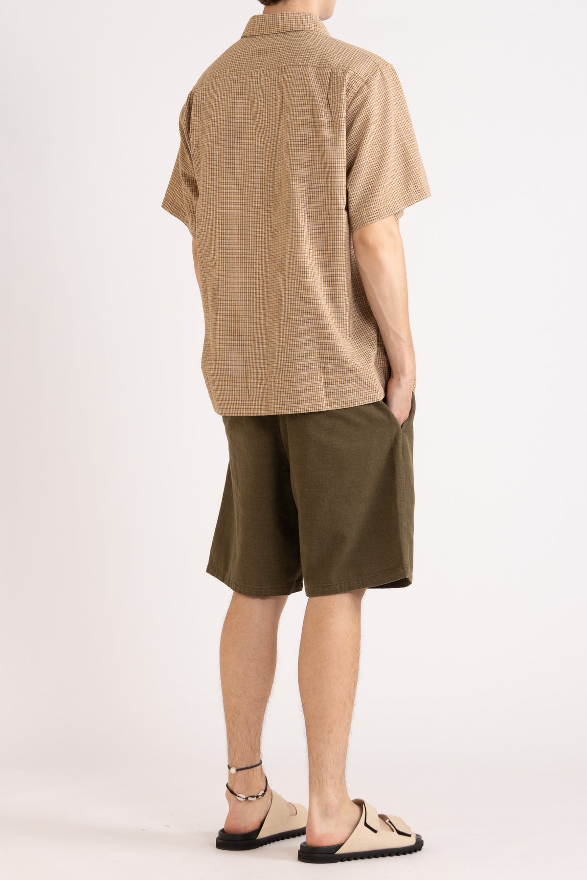 Model wearing a camel check cotton shirt and olive cotton shorts on a white background, side back view