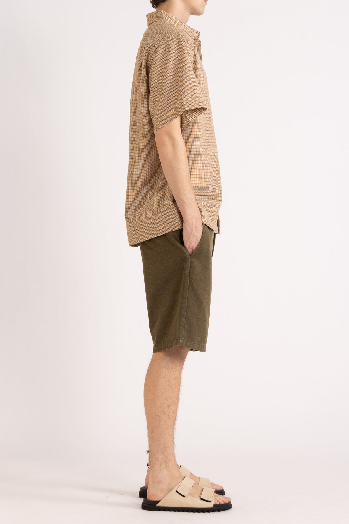 Model wearing a camel check cotton shirt and olive cotton shorts on a white background, side view