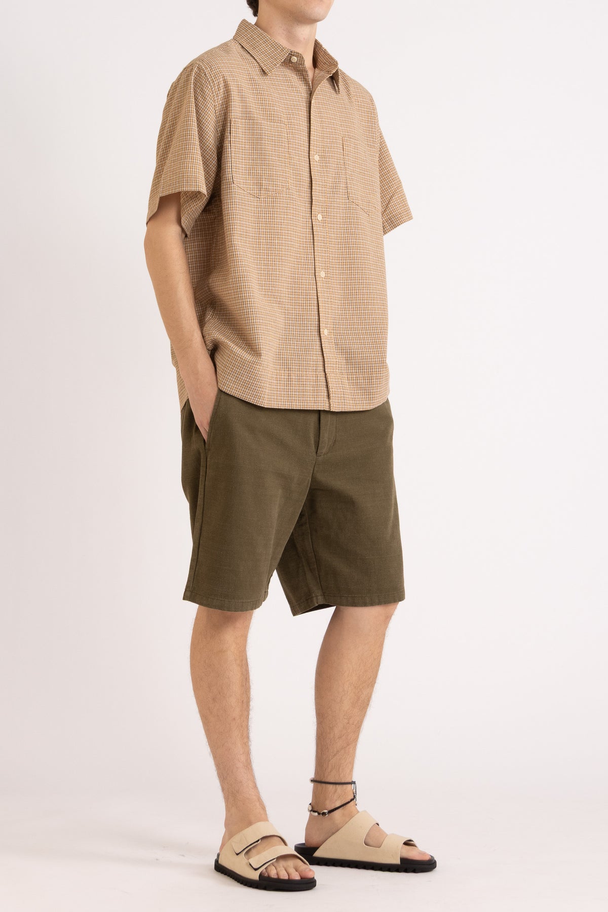 Model wearing a camel check cotton shirt and olive cotton shorts on a white background, front side view