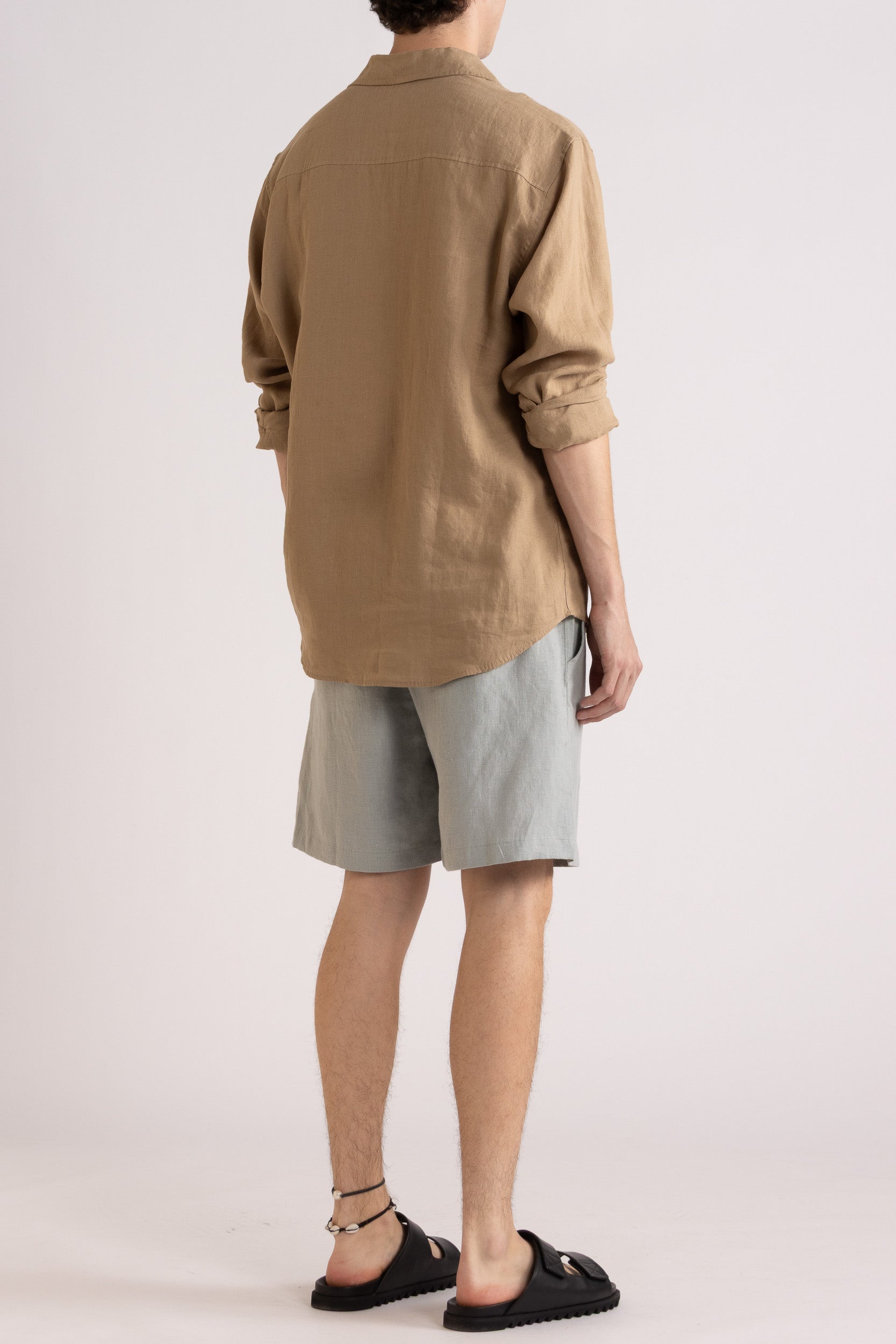 Model wearing a mocha linen shirt and light blue linen shorts on a white background, back side view