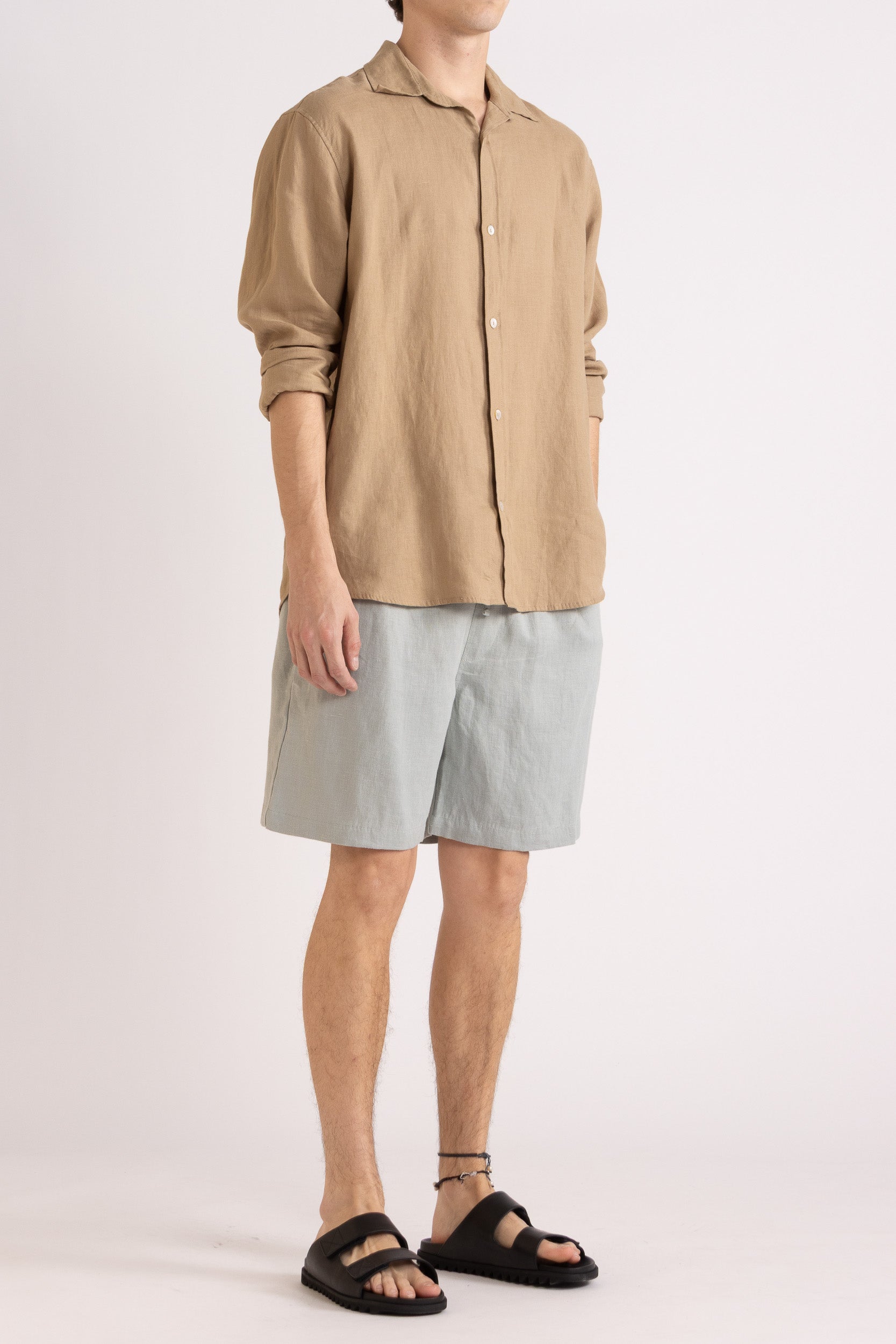 Model wearing a mocha linen shirt and light blue linen shorts on a white background, front side view