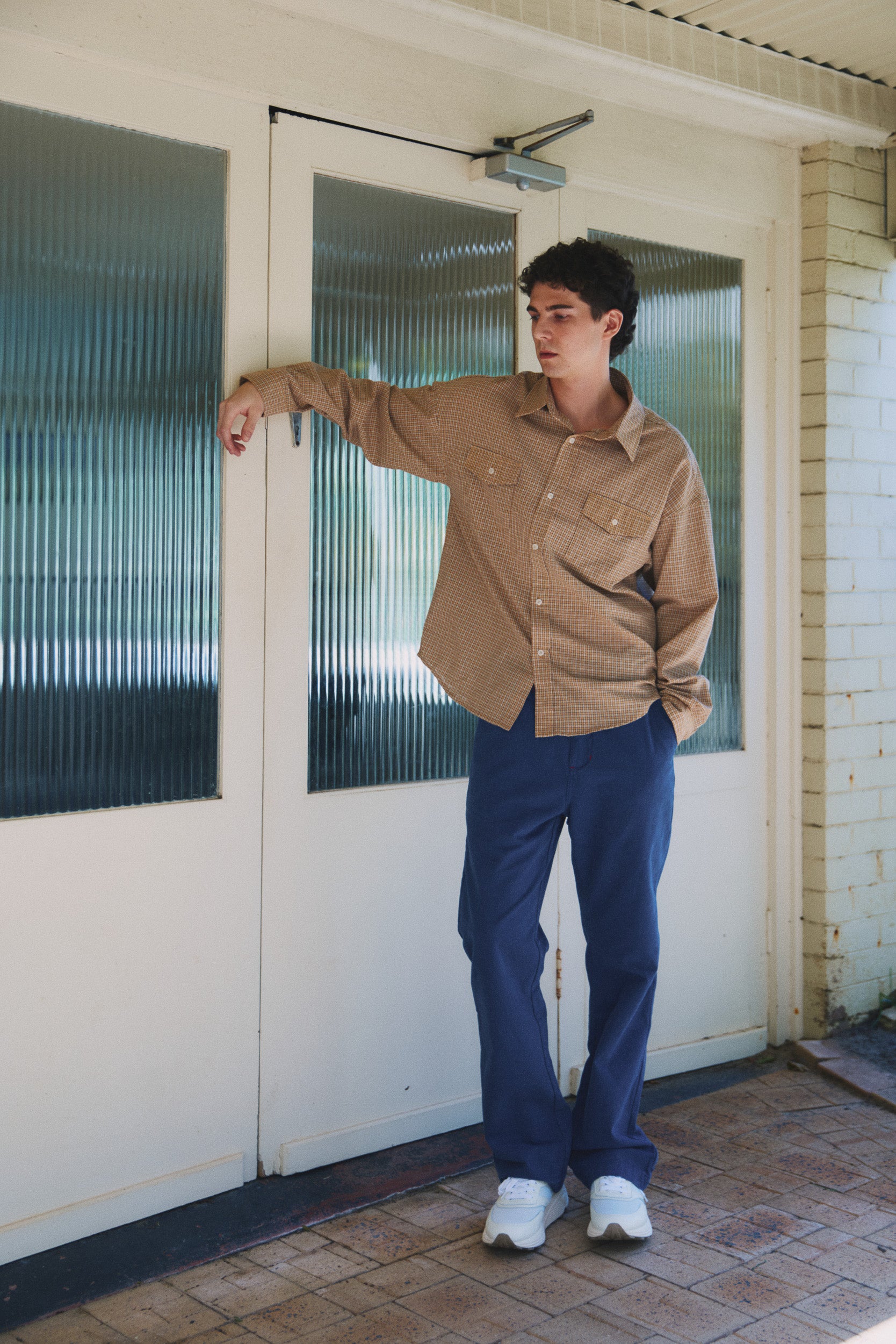 Model wearing a camel check shirt and blue cotton pants with white sneakers, campaign image