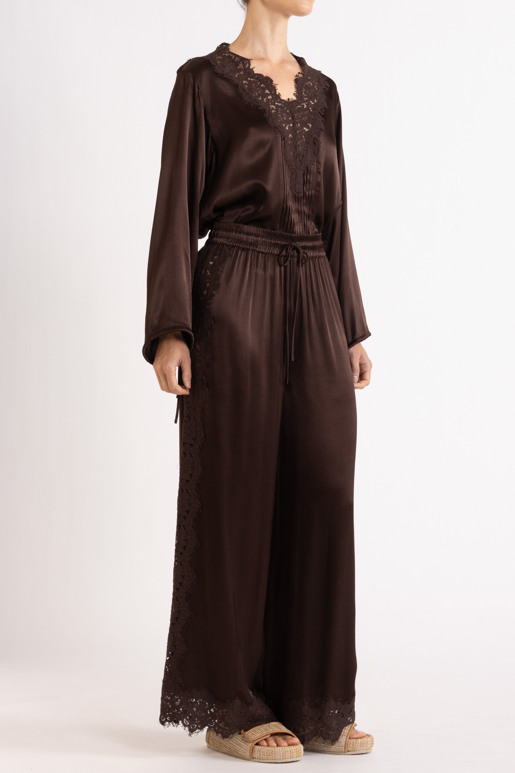 Woman wearing a brown long sleeve top and pant with lace details on a white background