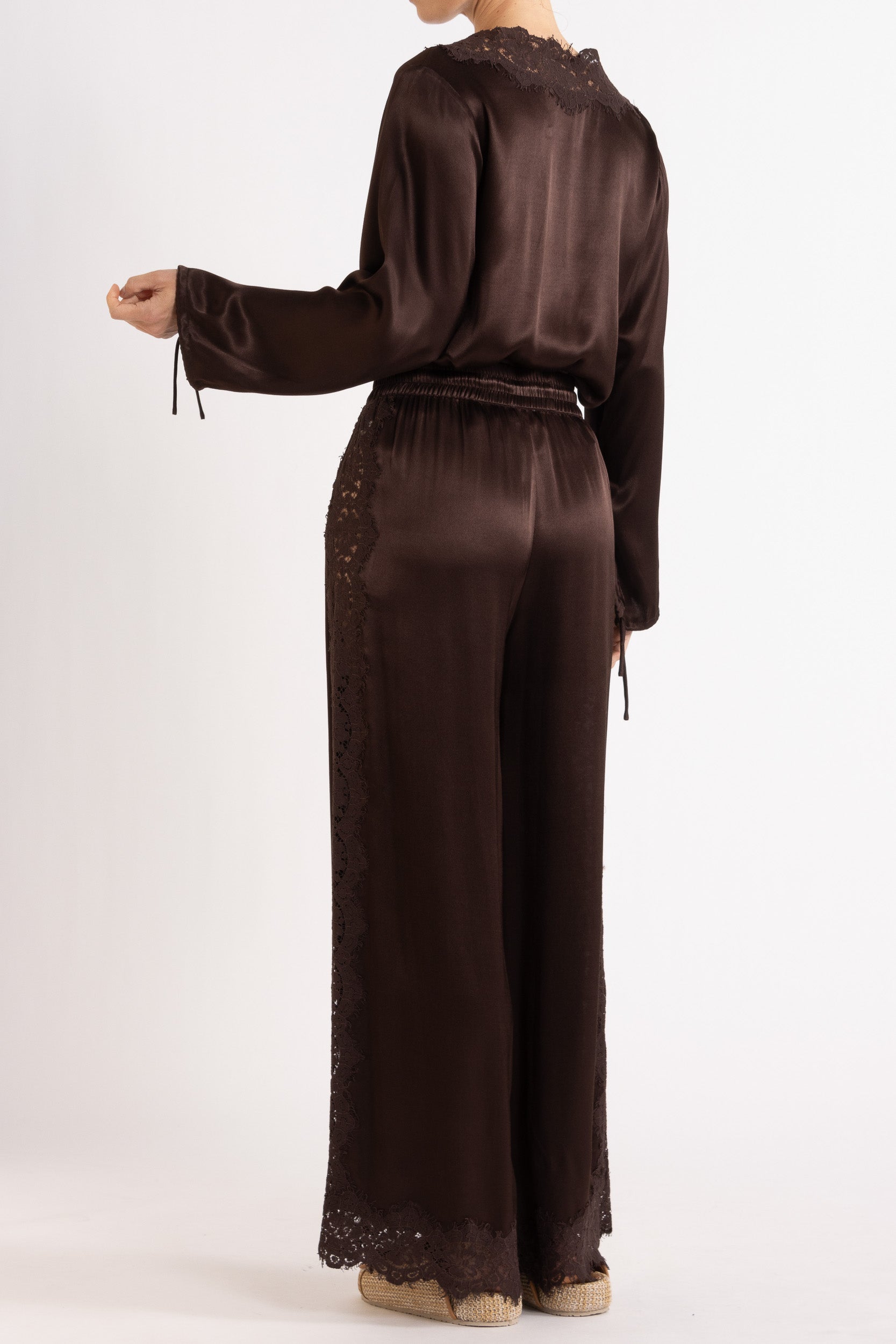 Woman wearing a brown long sleeve top and pant with lace details on a white background