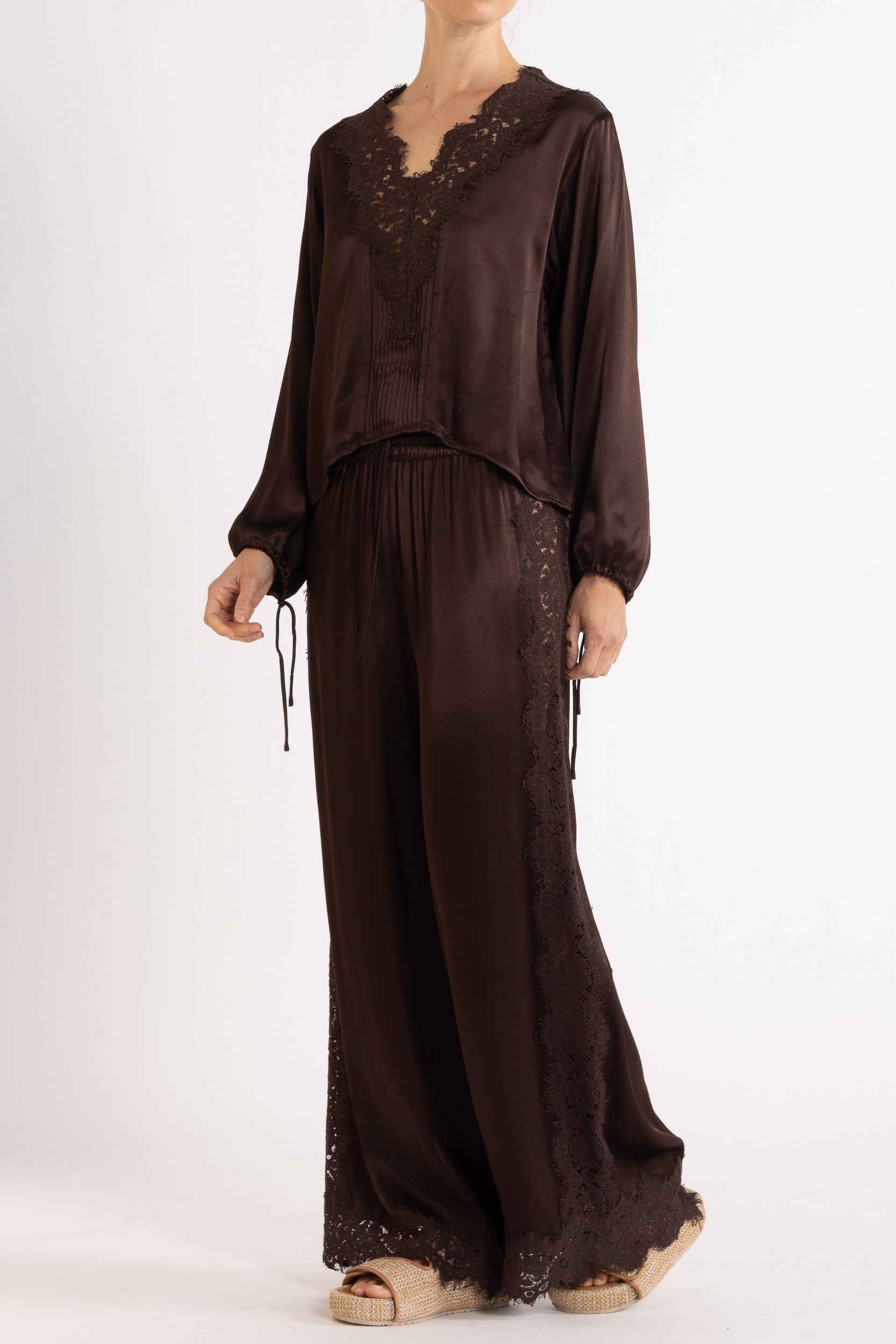 Woman wearing a brown long sleeve top and pant with lace details on a white background