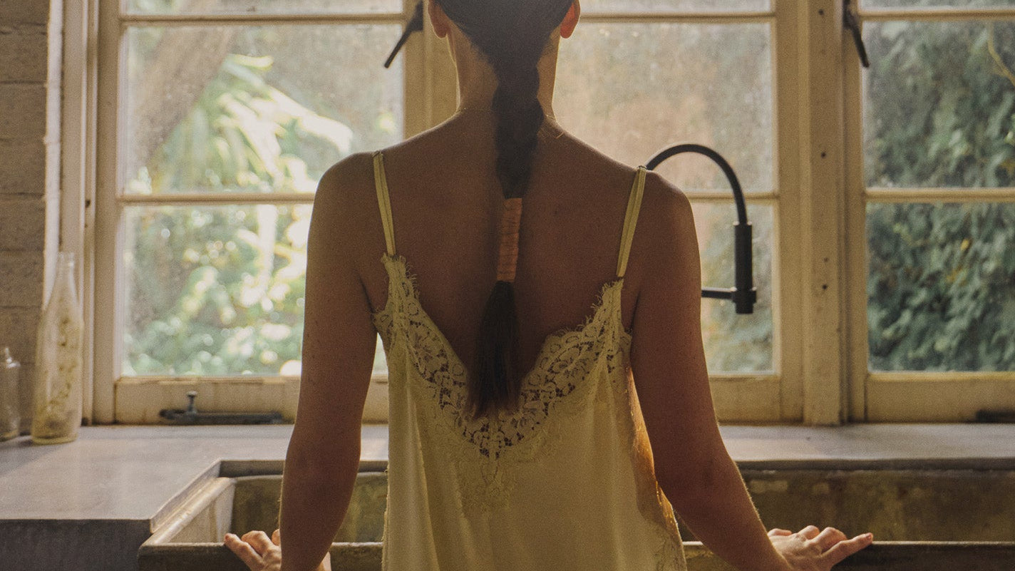 Woman in a vanilla-colored lace dress standing in an old kitchen with large windows.