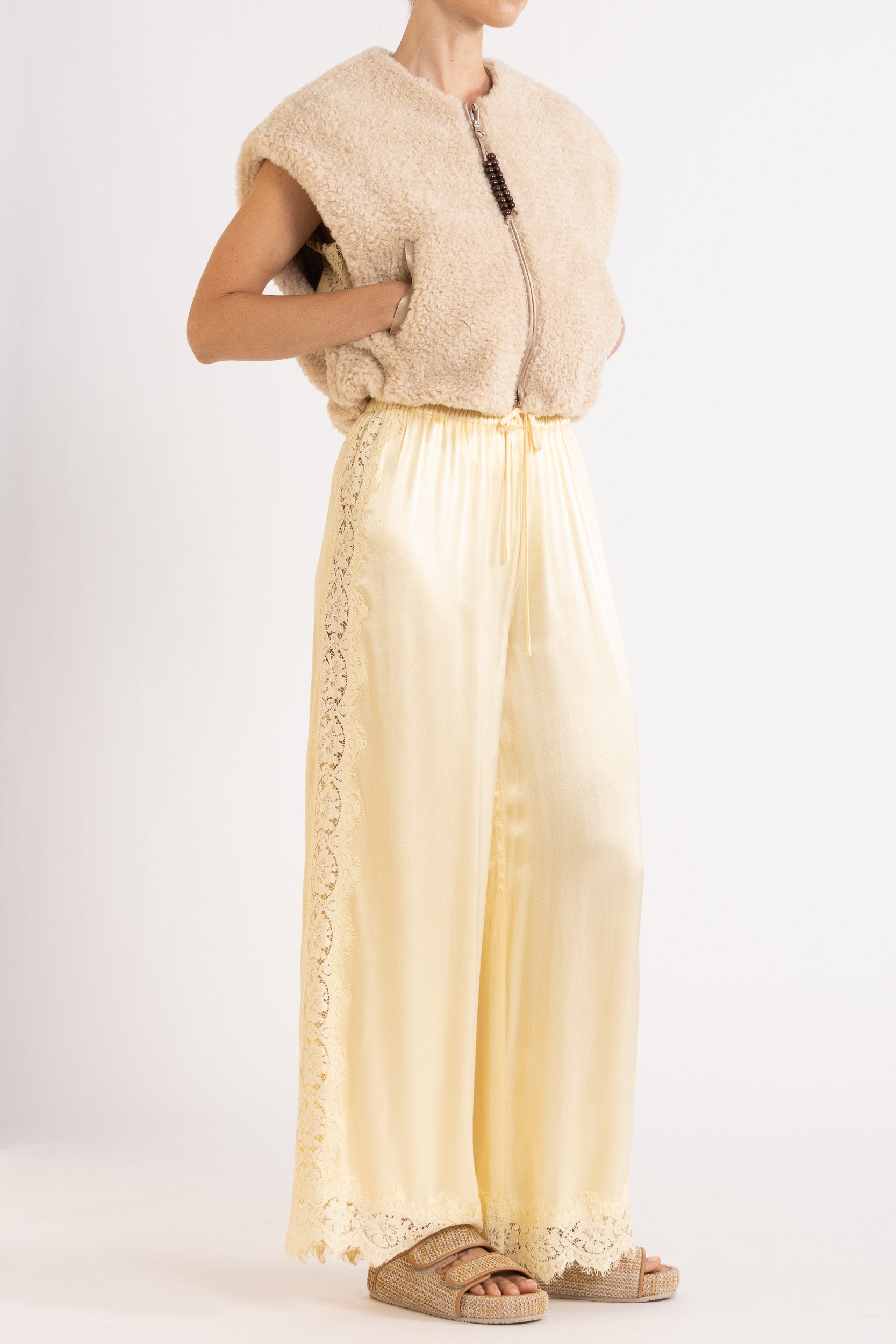 Woman wearing oat colour faux fur zip up vest with vanilla lace-trimmed pants
