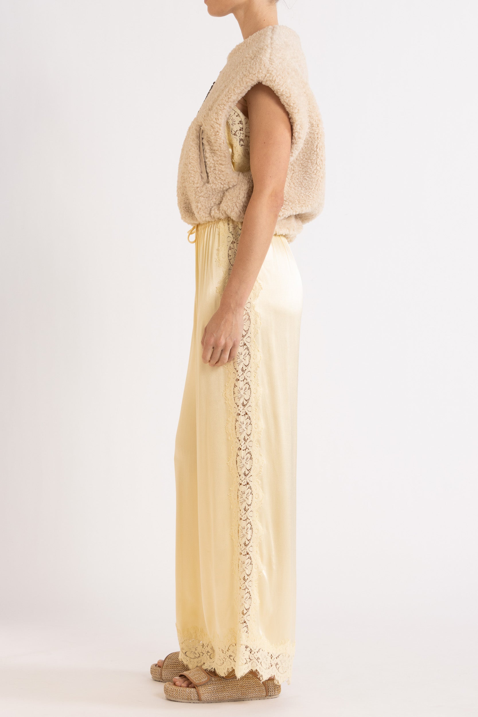 Woman wearing oat colour faux fur zip up vest with vanilla lace-trimmed pants