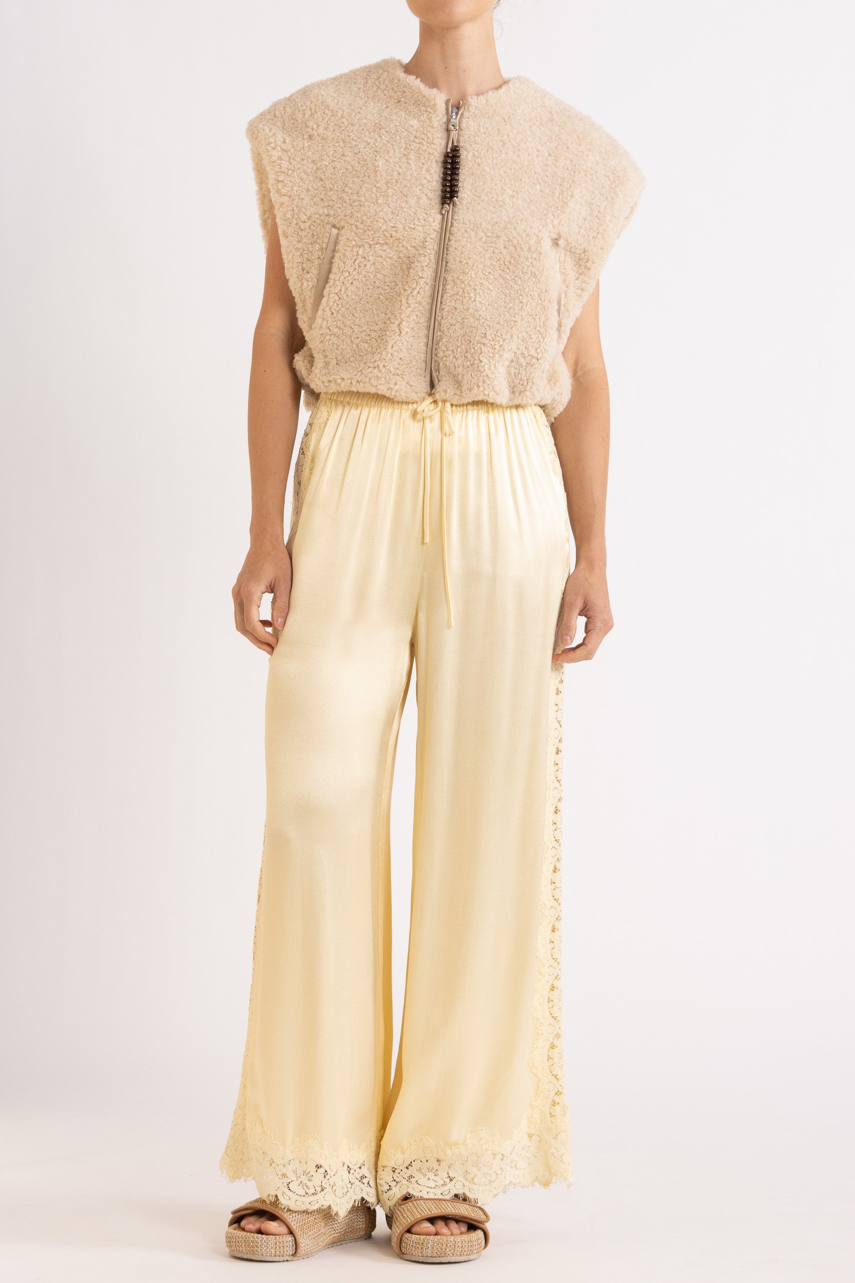 Woman wearing oat colour faux fur zip up vest with vanilla lace-trimmed pants