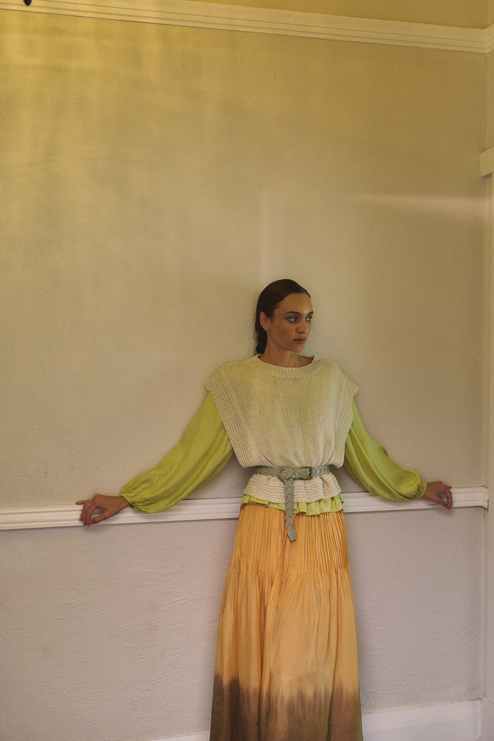 Woman wearing oat linen vest layered over a vanilla long sleeve top, paired over a light orange dip dyed maxi skirt with a cream braided belt.