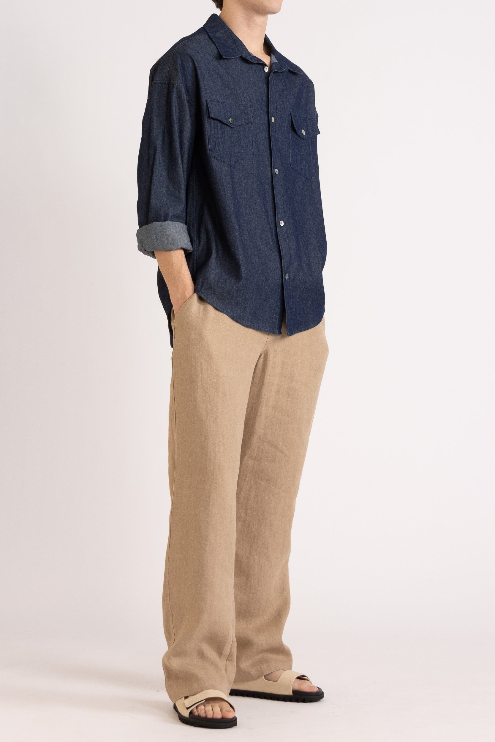 Model wearing a navy blue shirt and mocha linen pants on a white background, front side view