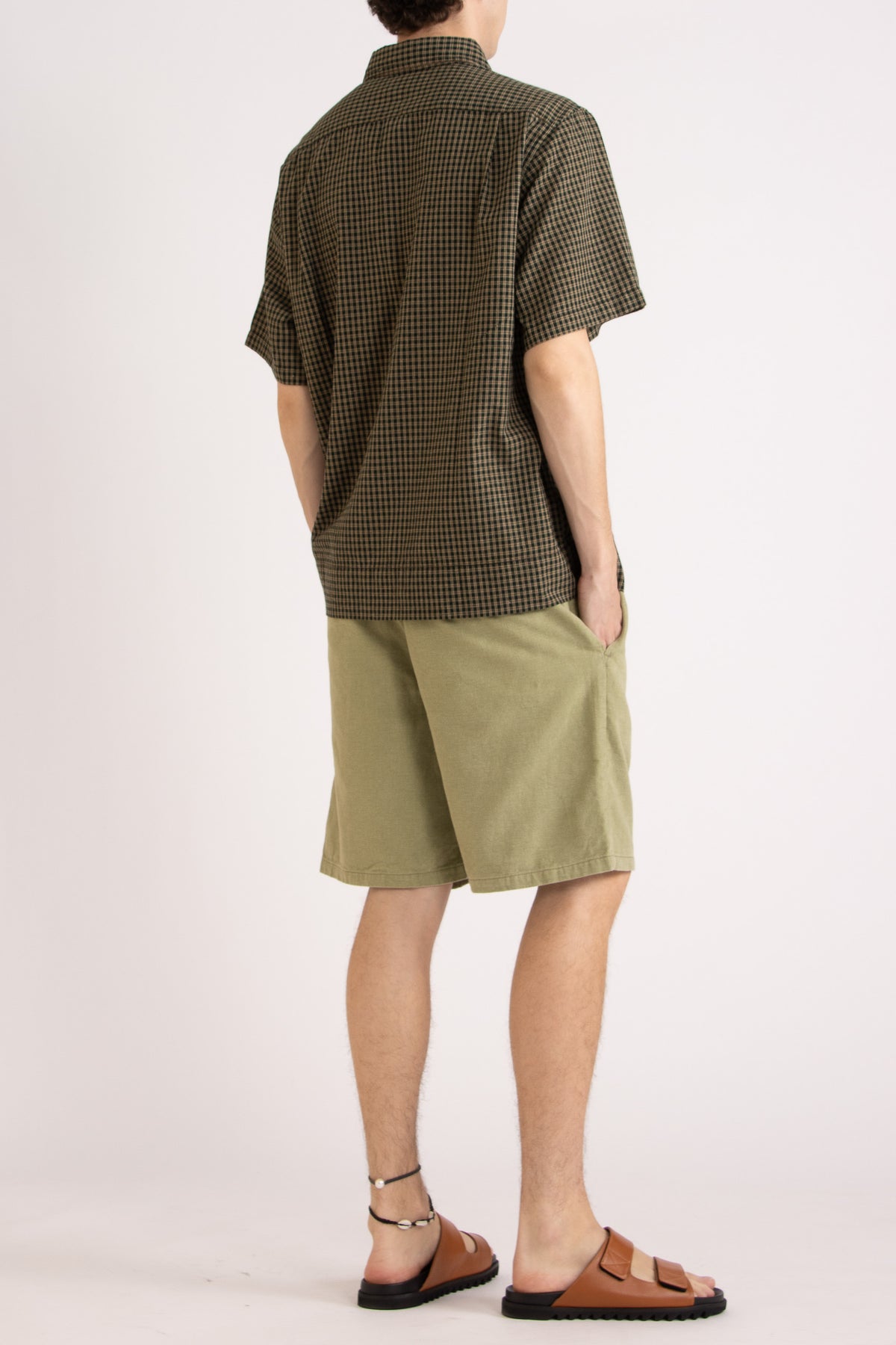 Model wearing a green check cotton shirt and green cotton shorts on a white background, side back view