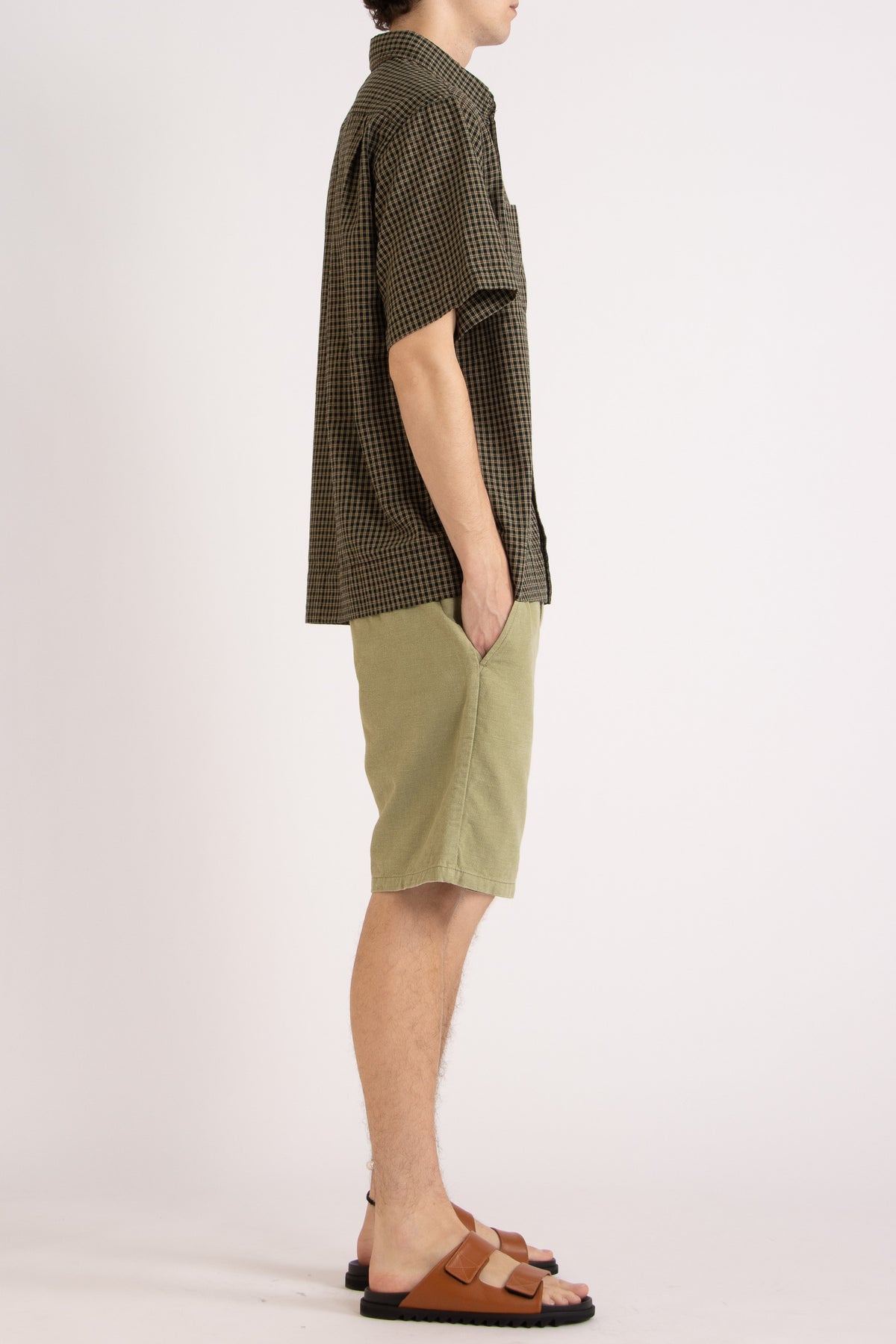 Model wearing a green check cotton shirt and green cotton shorts on a white background, side view