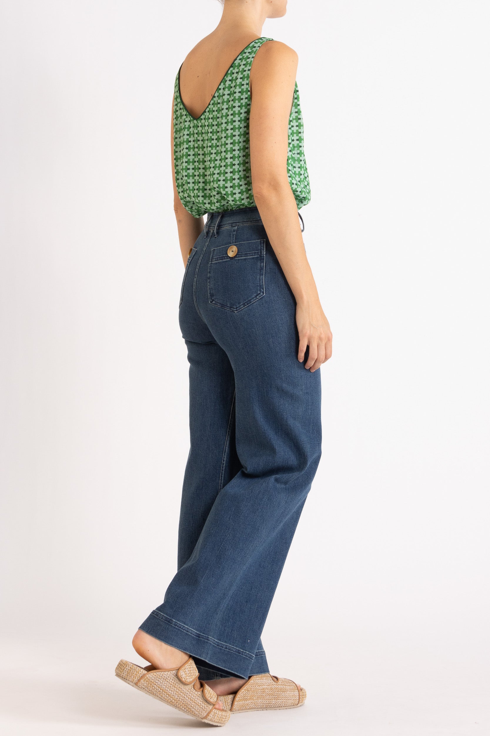 Model wearing green patterned tank top and high-waisted jeans, side-back view