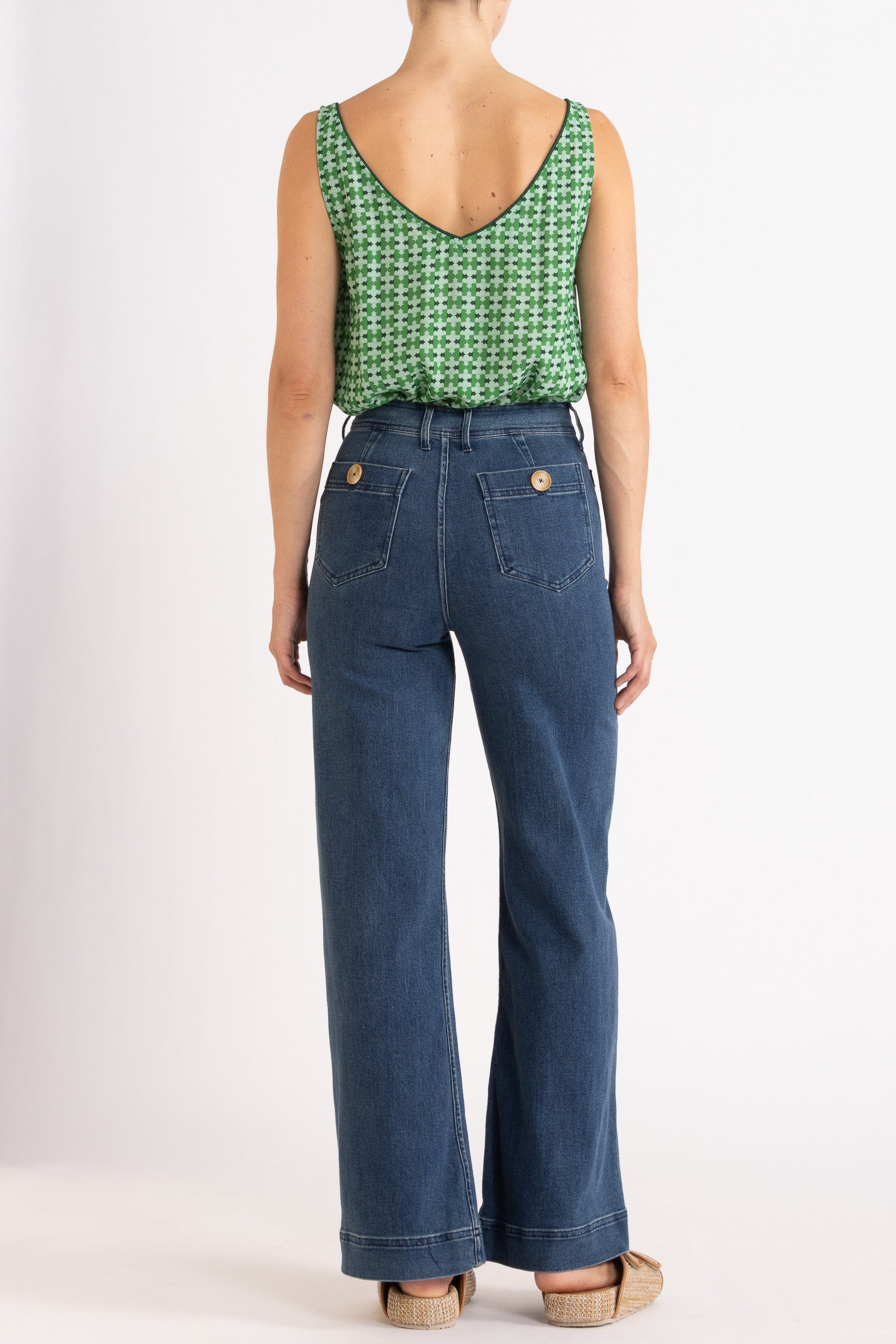 Model wearing green patterned tank top and high-waisted jeans, back view
