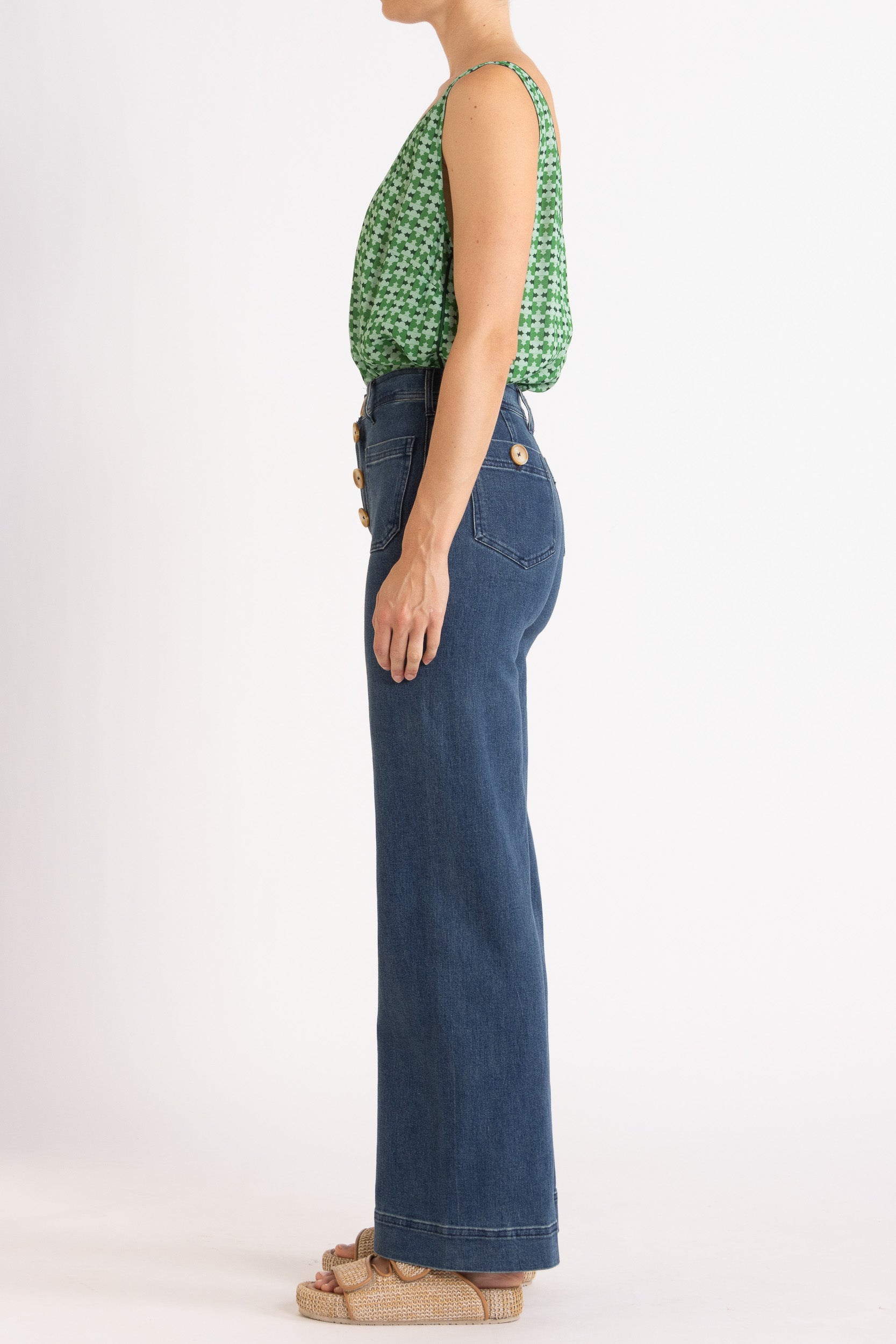 Model wearing green patterned tank top and high-waisted jeans, side view