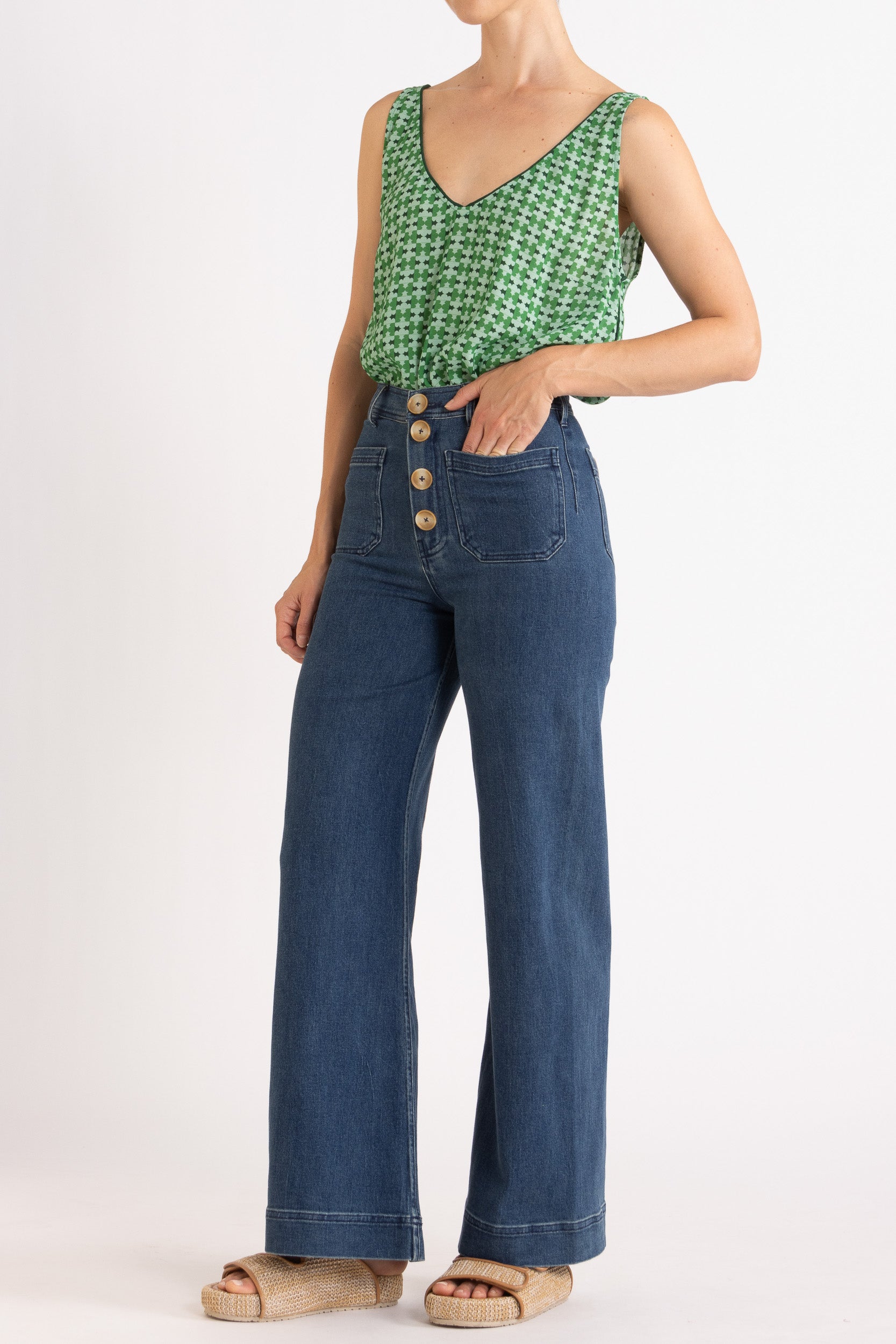 Model wearing green patterned tank top and high-waisted jeans, front-side view