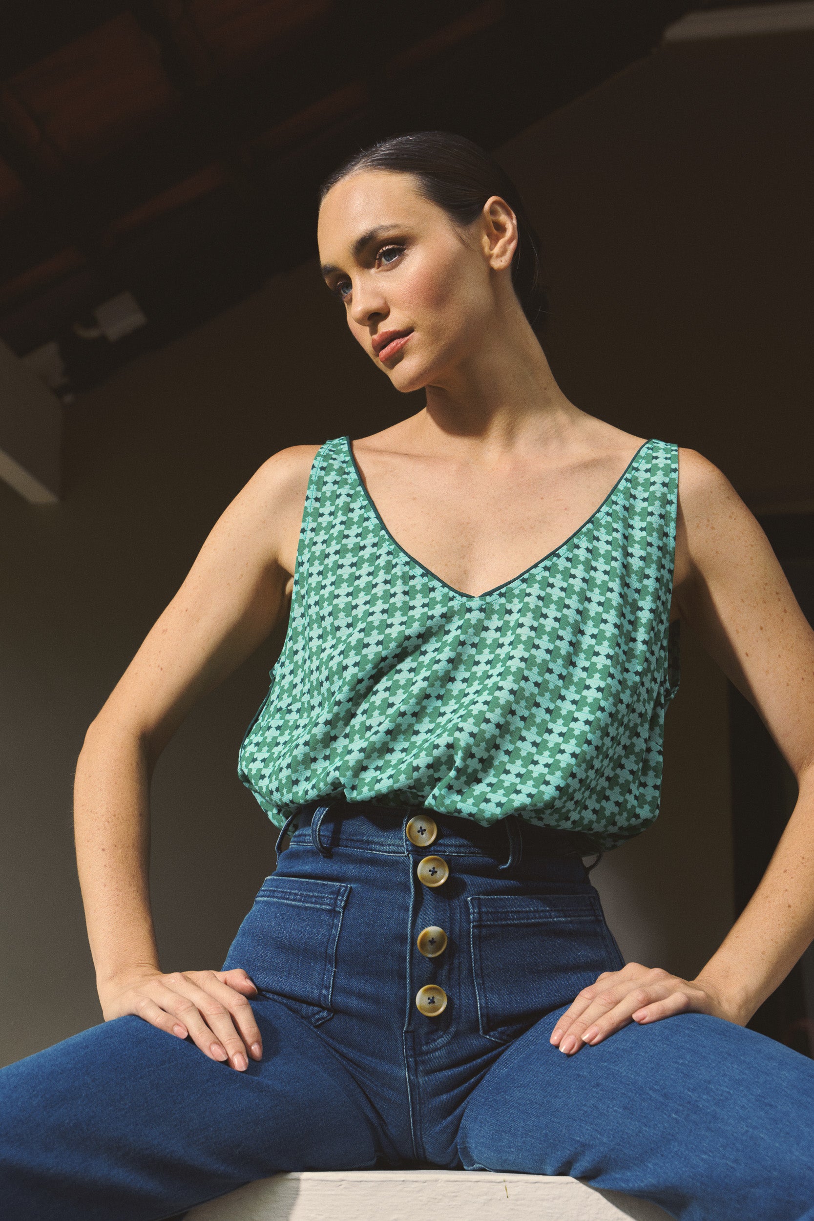 Model wearing green patterned tank top and high-waisted jeans, close-up campaign image
