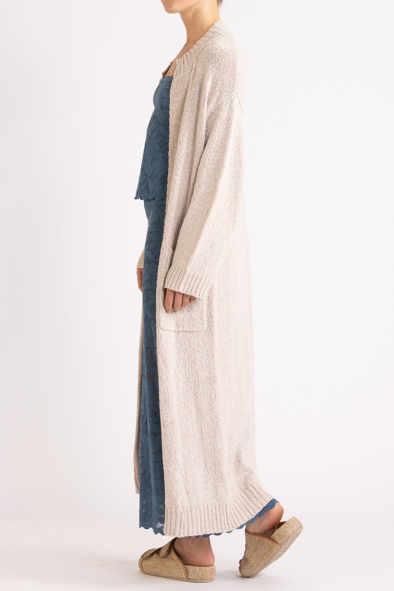 Model wearing beige knitted longline cardigan, navy stretch lace camisole and skirt, side view