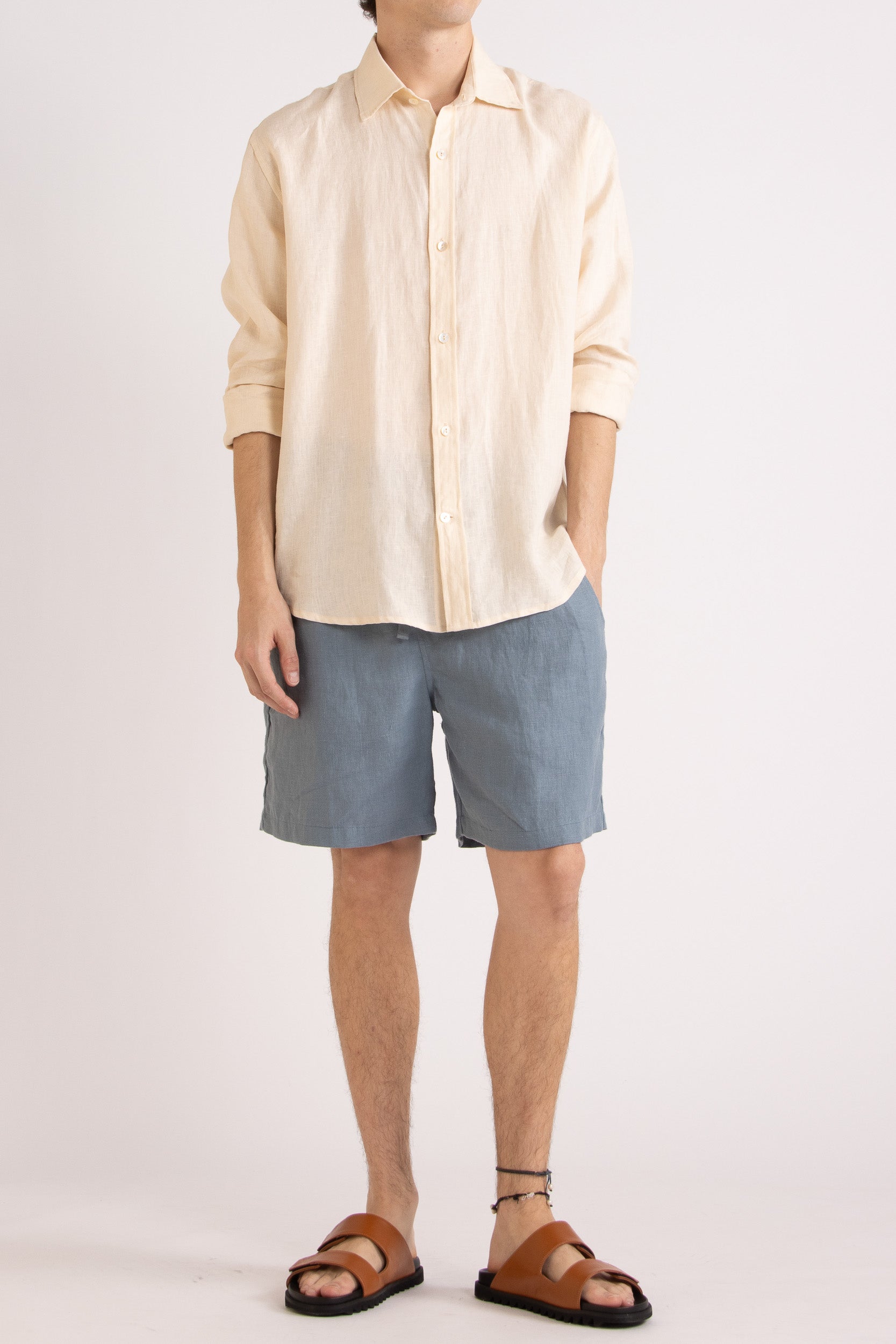 Model wearing a natural linen long sleeve shirt and steel blue linen shorts on a white background, front view.