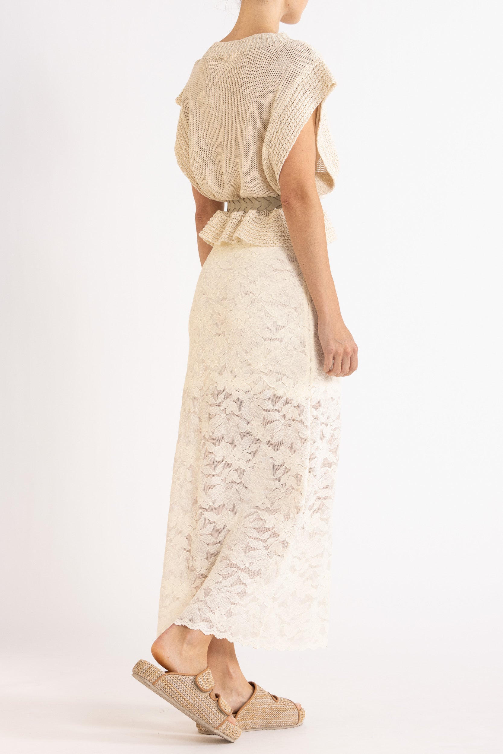 Woman wearing an Oat linen vest with a braided cream belt and a white floral lace maxi skirt